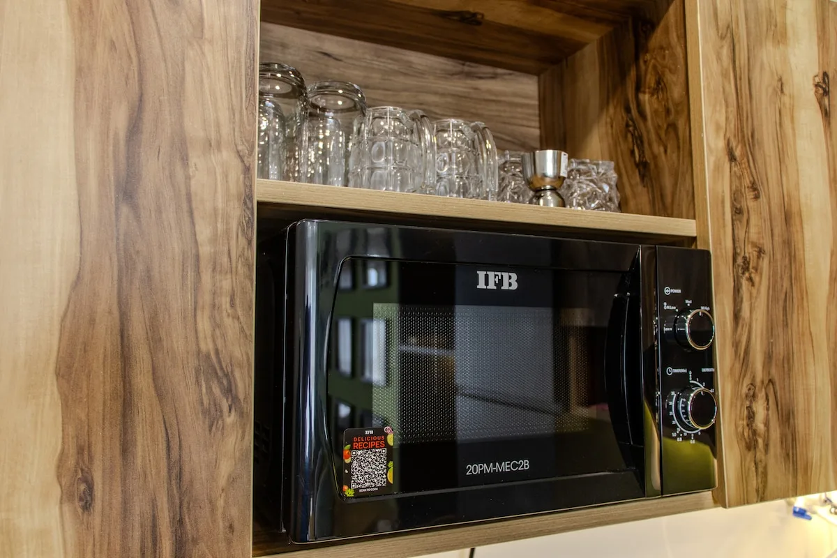 Un microondas está en un armario de cocina de madera, debajo de una repisa con cristalería.