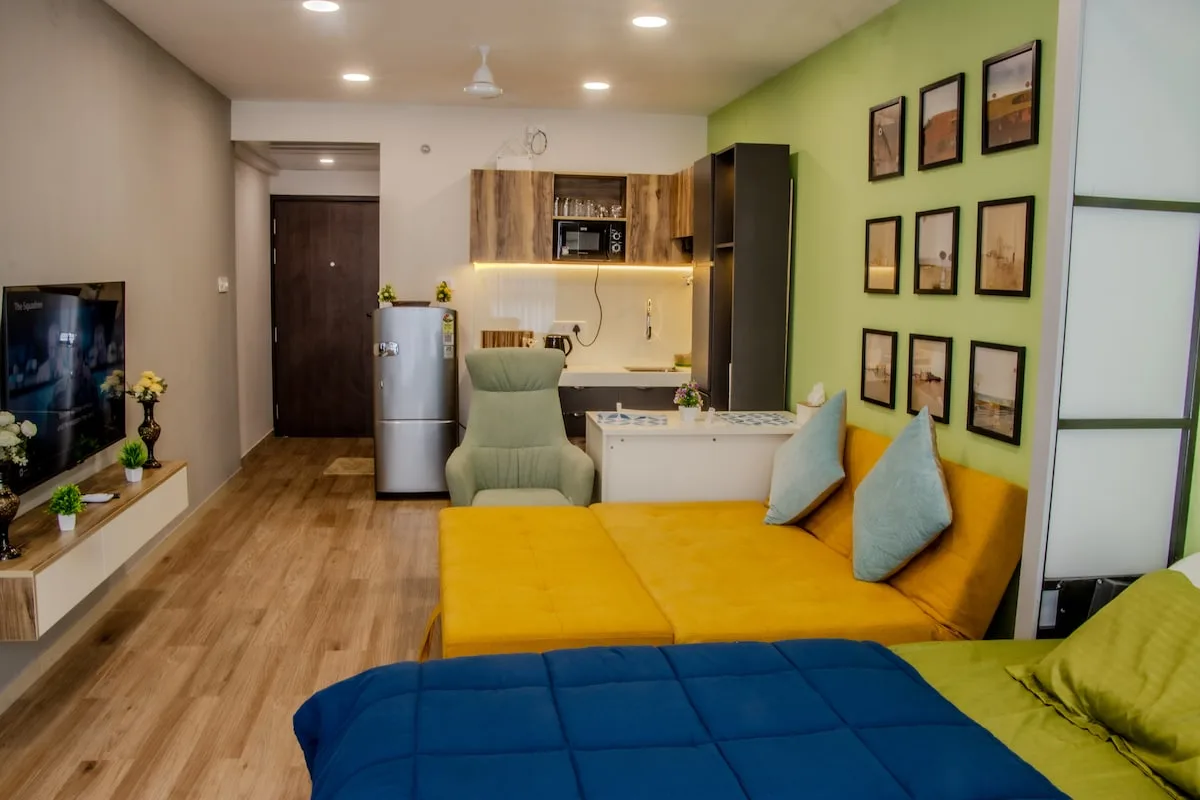 Una sala compacta con un sofá amarillo y una pequeña cocina al fondo.