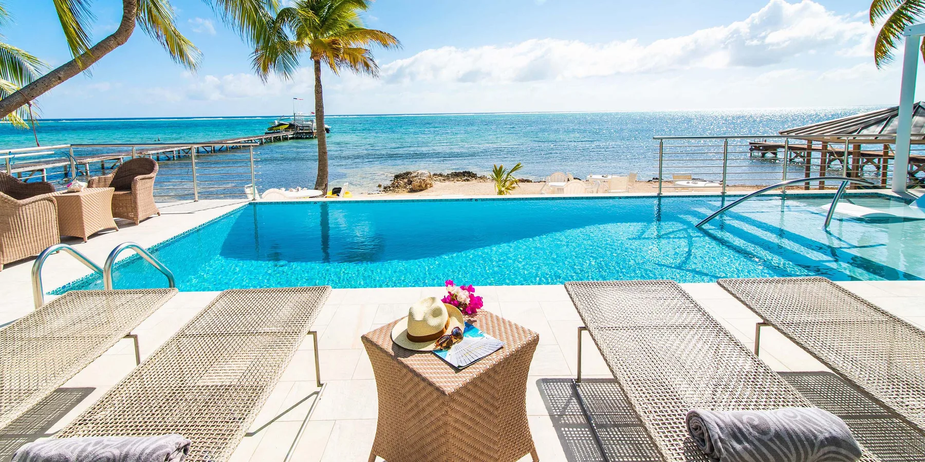 Una terraza junto a la piscina mira al océano, con asientos y palmeras.
