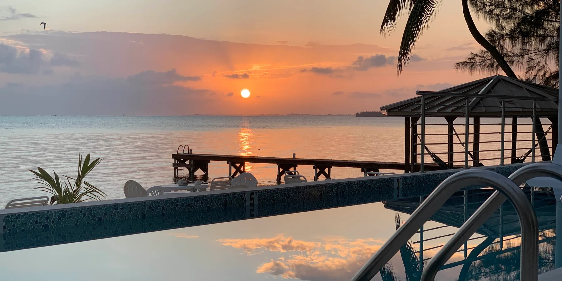 Una piscina da a un mar en calma al atardecer, con una terraza de madera junto al agua.