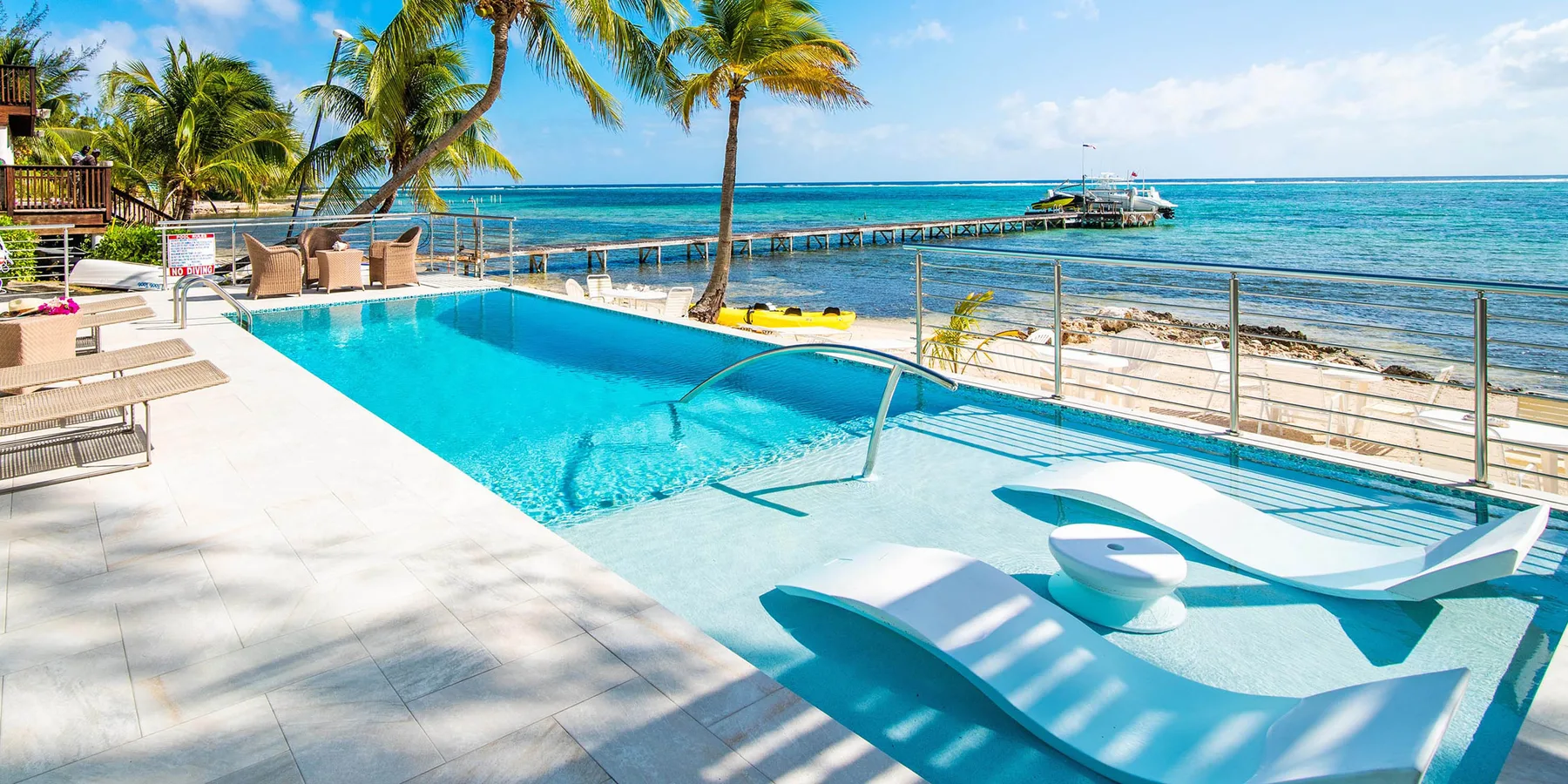 Una piscina junto al mar con tumbonas y palmeras junto al océano.