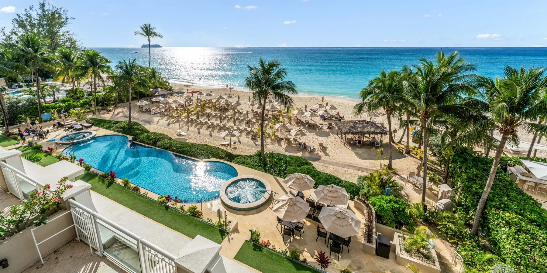 Una piscina de resort da a una playa de arena bordeada de palmeras.