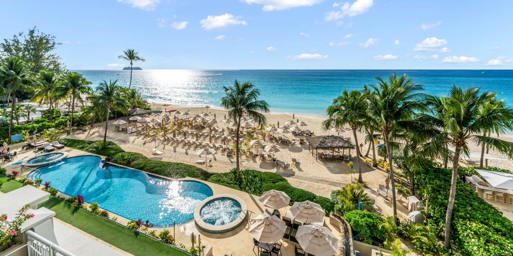 Un resort tropical frente al mar, con una piscina curva junto a una playa de arena.