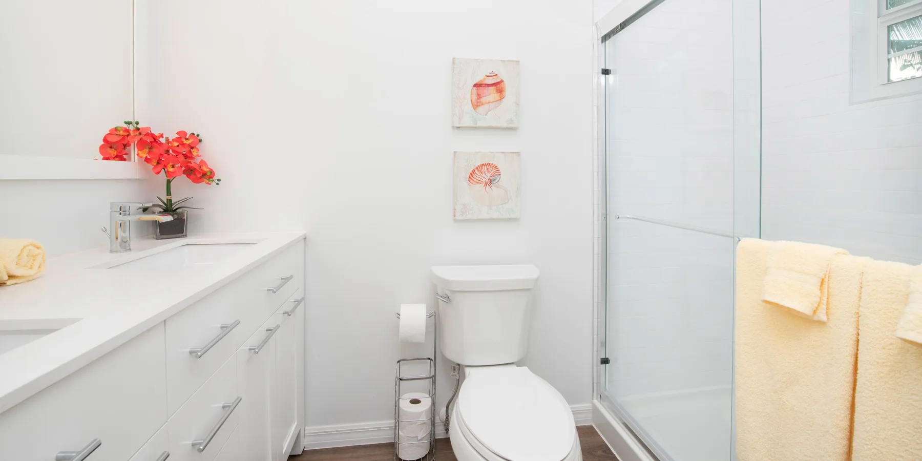 Un baño luminoso con lavabo blanco, inodoro y ducha de vidrio.
