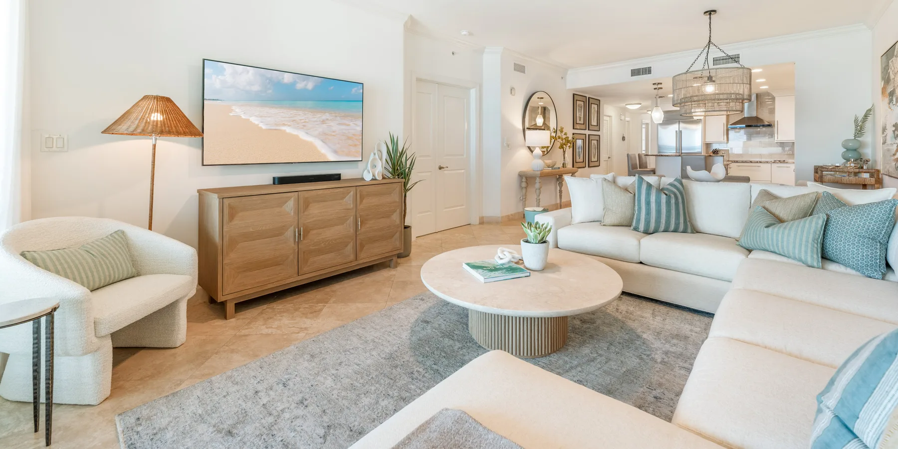 Una sala luminosa con asientos claros, un mueble de madera y una cocina abierta.