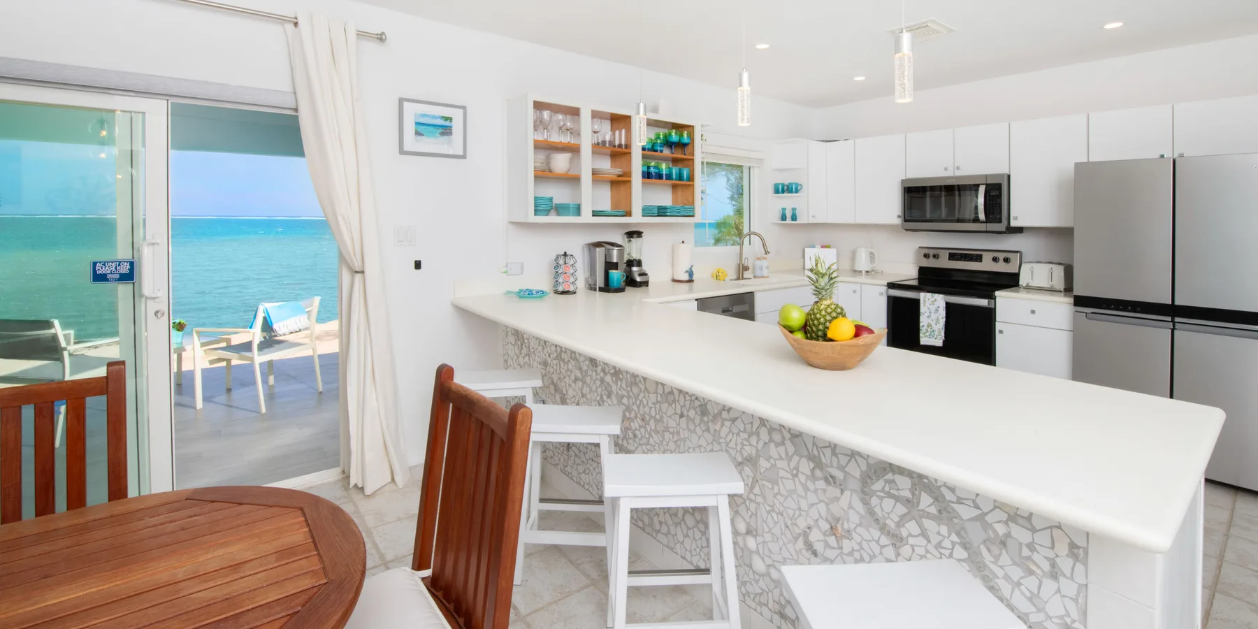 Una cocina luminosa y abierta con una barra larga y puertas corredizas de vidrio con vista al agua.