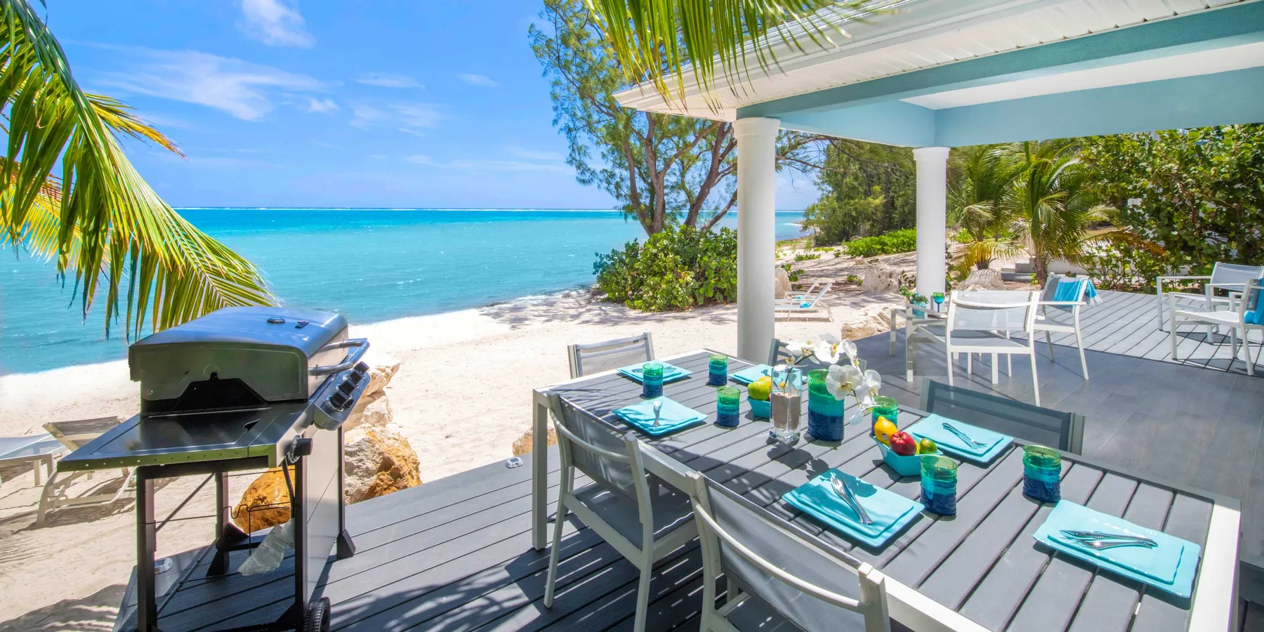 Un comedor junto al mar con una mesa puesta y una parrilla al lado de la playa.