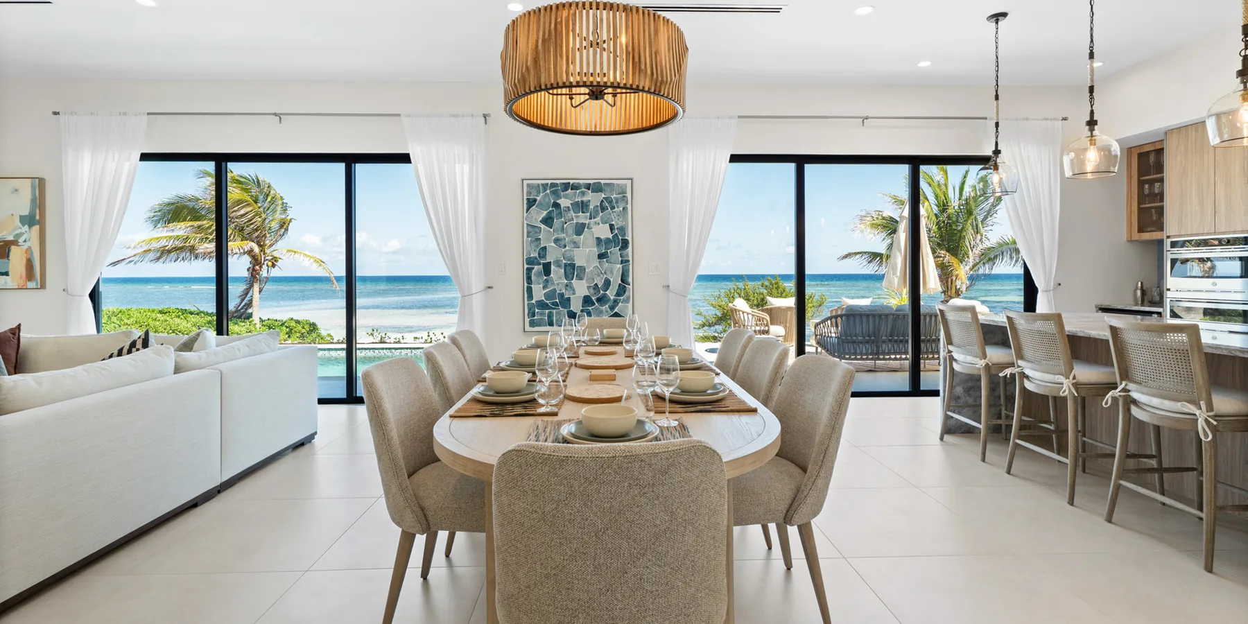 Un comedor luminoso con una mesa larga y asientos junto a grandes ventanas con vista al océano.