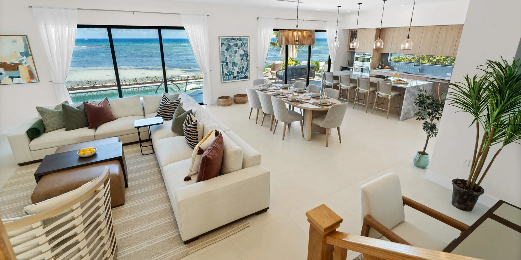 Una sala abierta con comedor y cocina, y grandes ventanas con vista al mar.