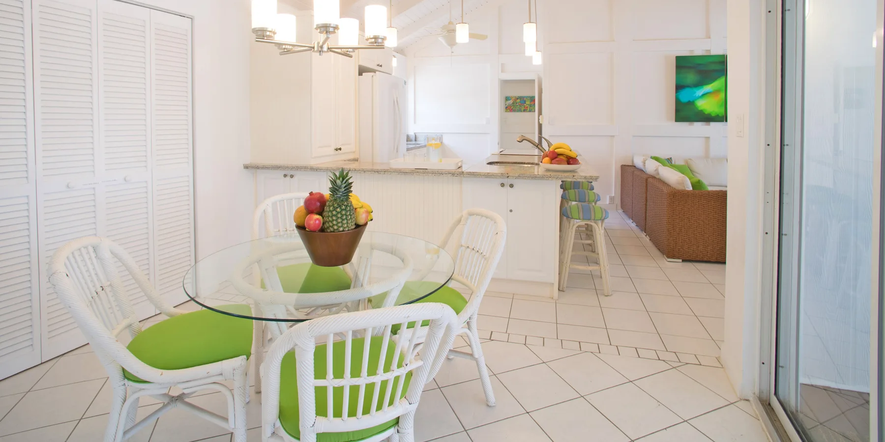 A bright dining area with a glass table and green-cushioned seating.