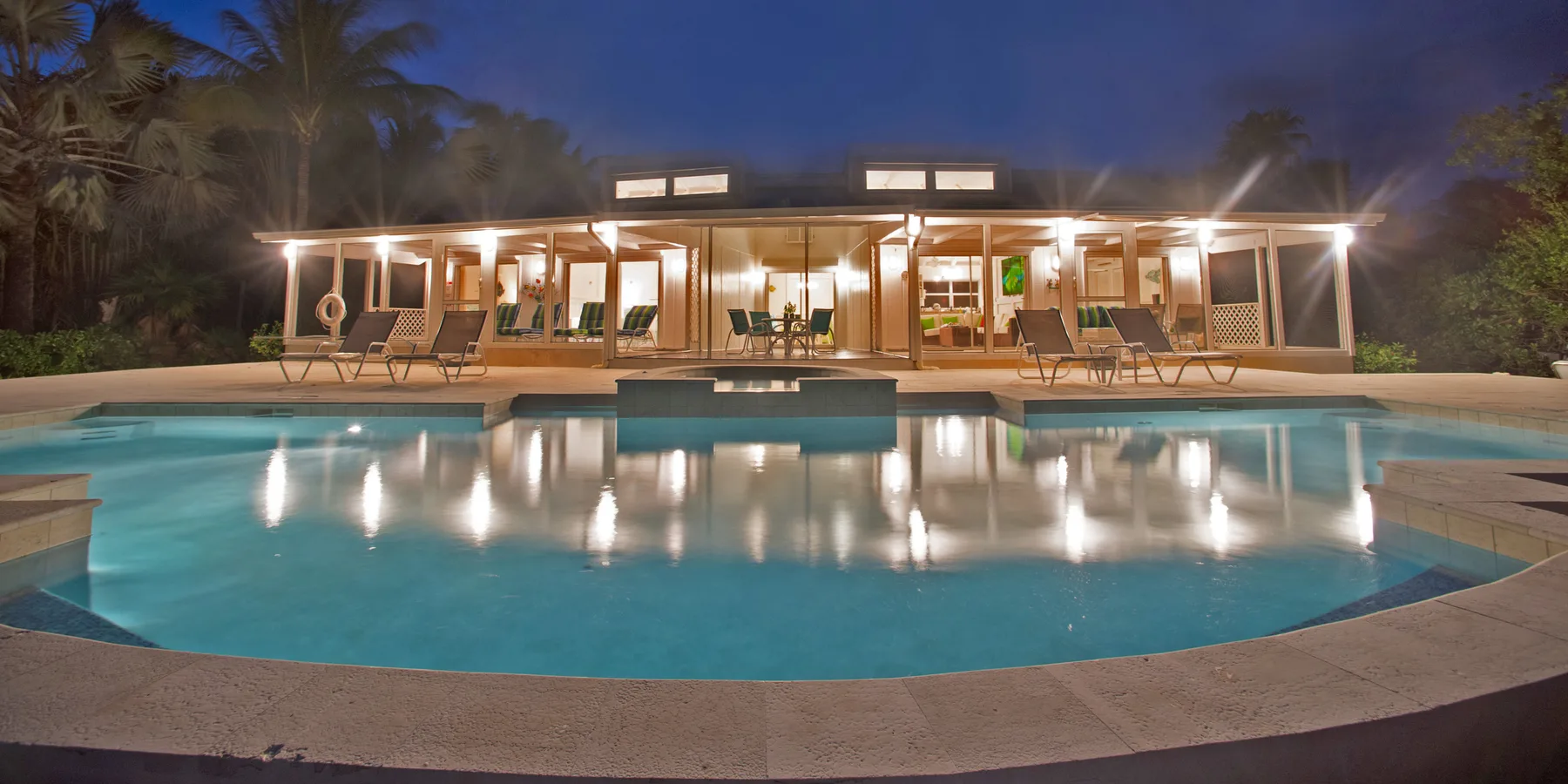 A swimming pool in front of a brightly lit, single-story building at night.