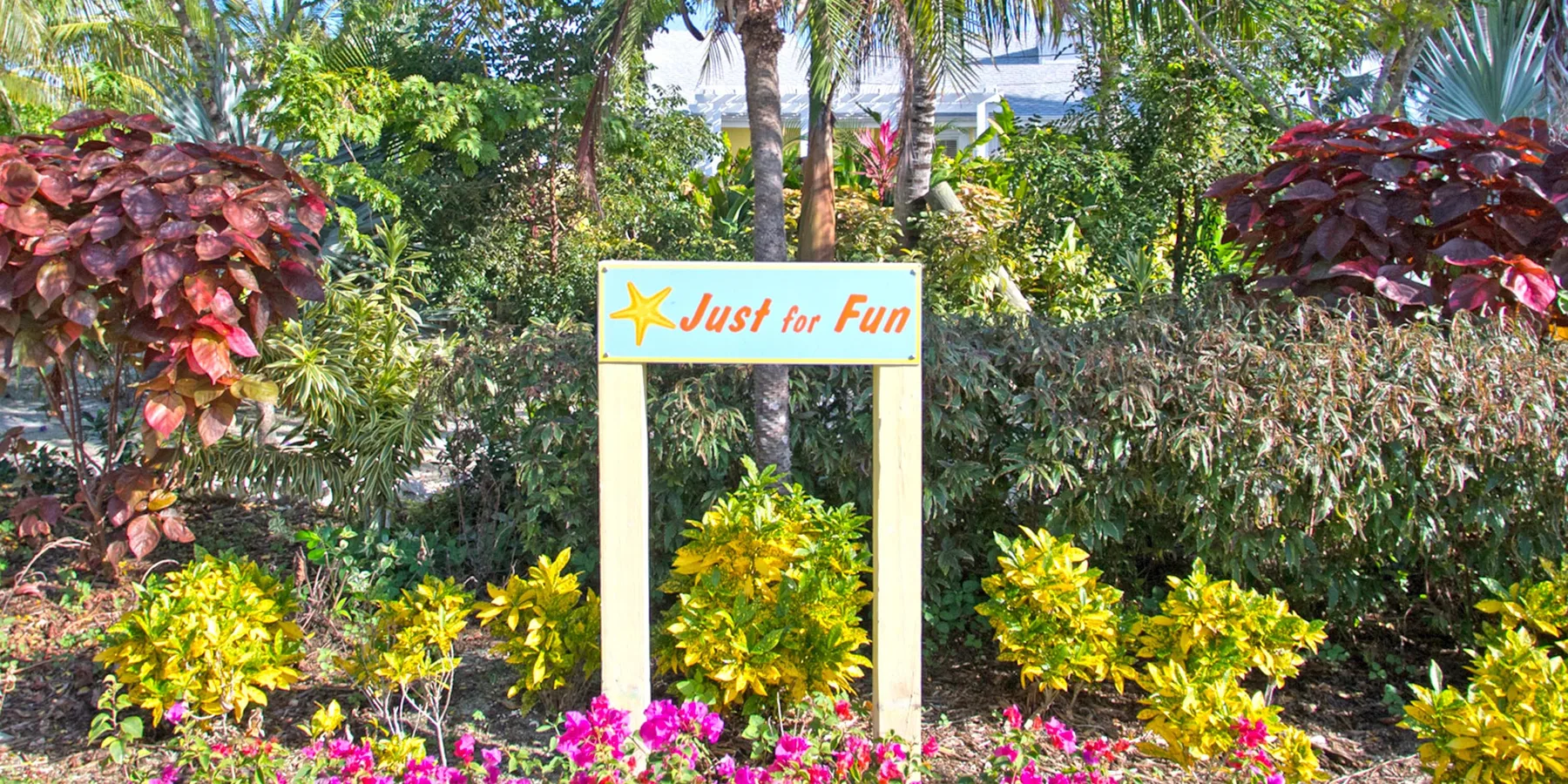 A tropical garden features colorful flowers and a sign that reads “Just for Fun.”