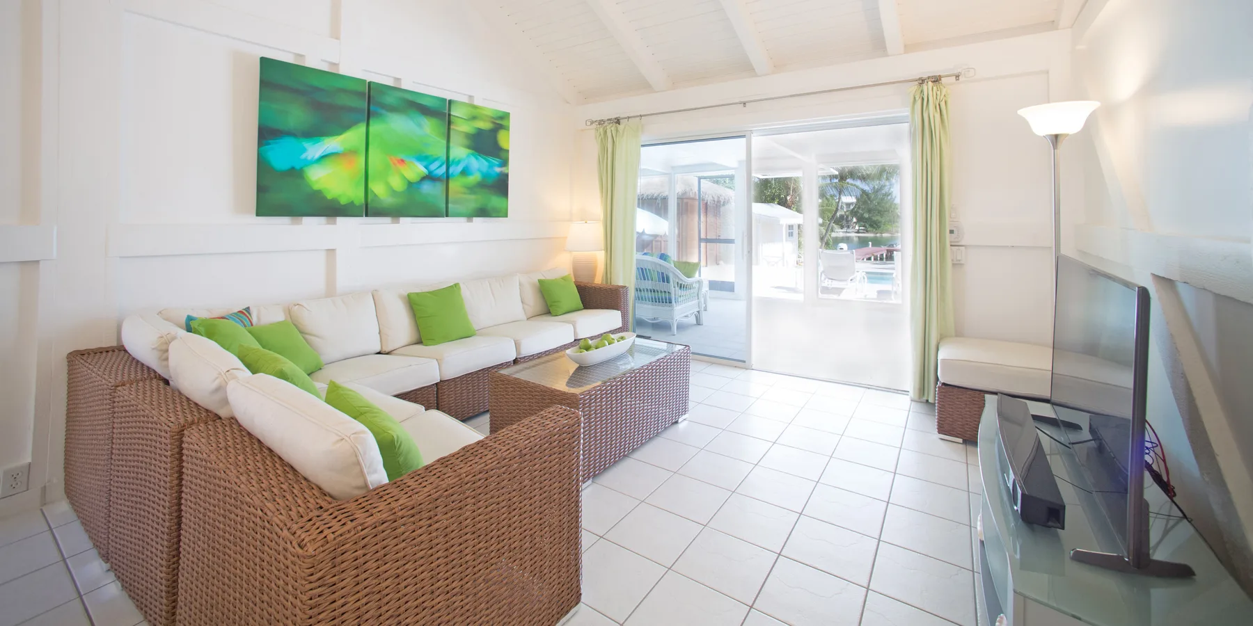 A bright living room with wicker seating, a television, and sliding glass doors.
