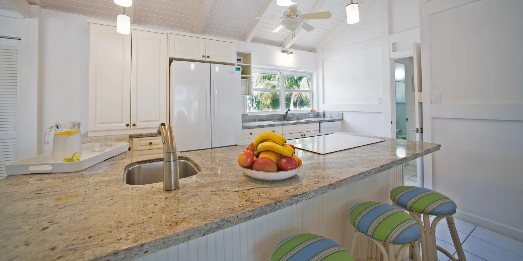 A bright kitchen with a large island, sink, and fruit bowl.