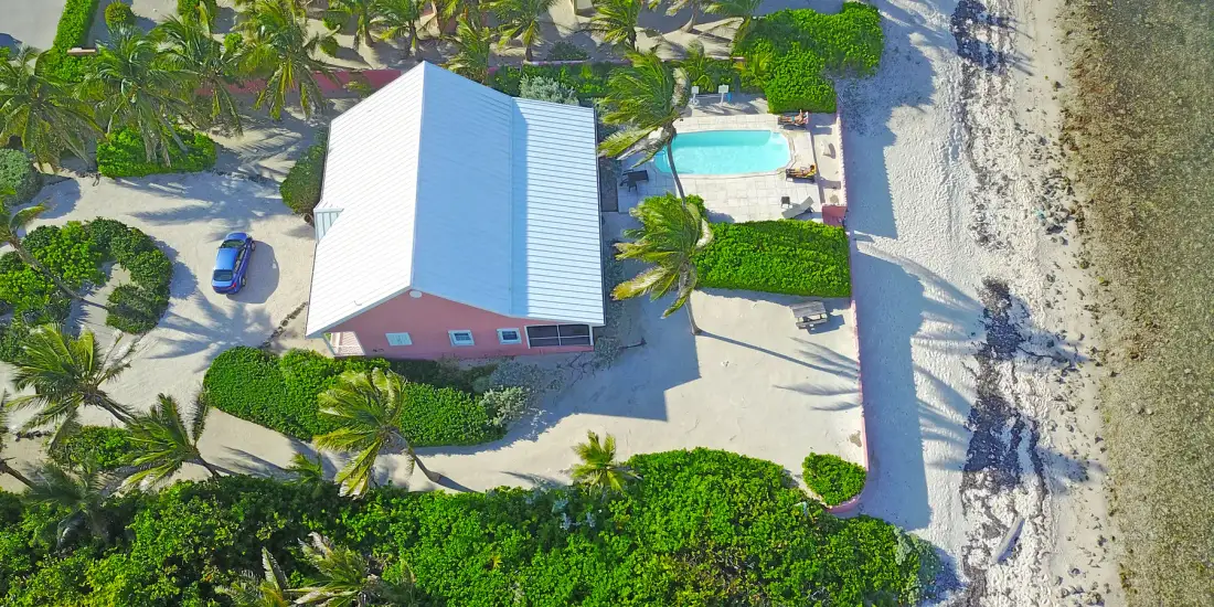 Una vista aérea muestra una propiedad junto a la playa, con una piscina al lado de la costa arenosa.