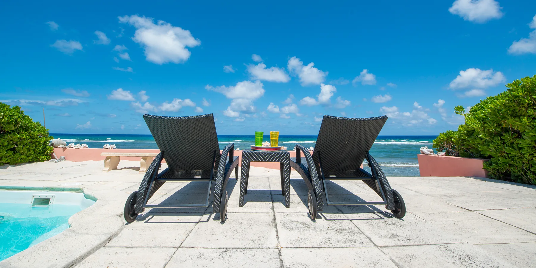 Un patio junto al mar tiene dos sillones y una mesa pequeña frente al océano.