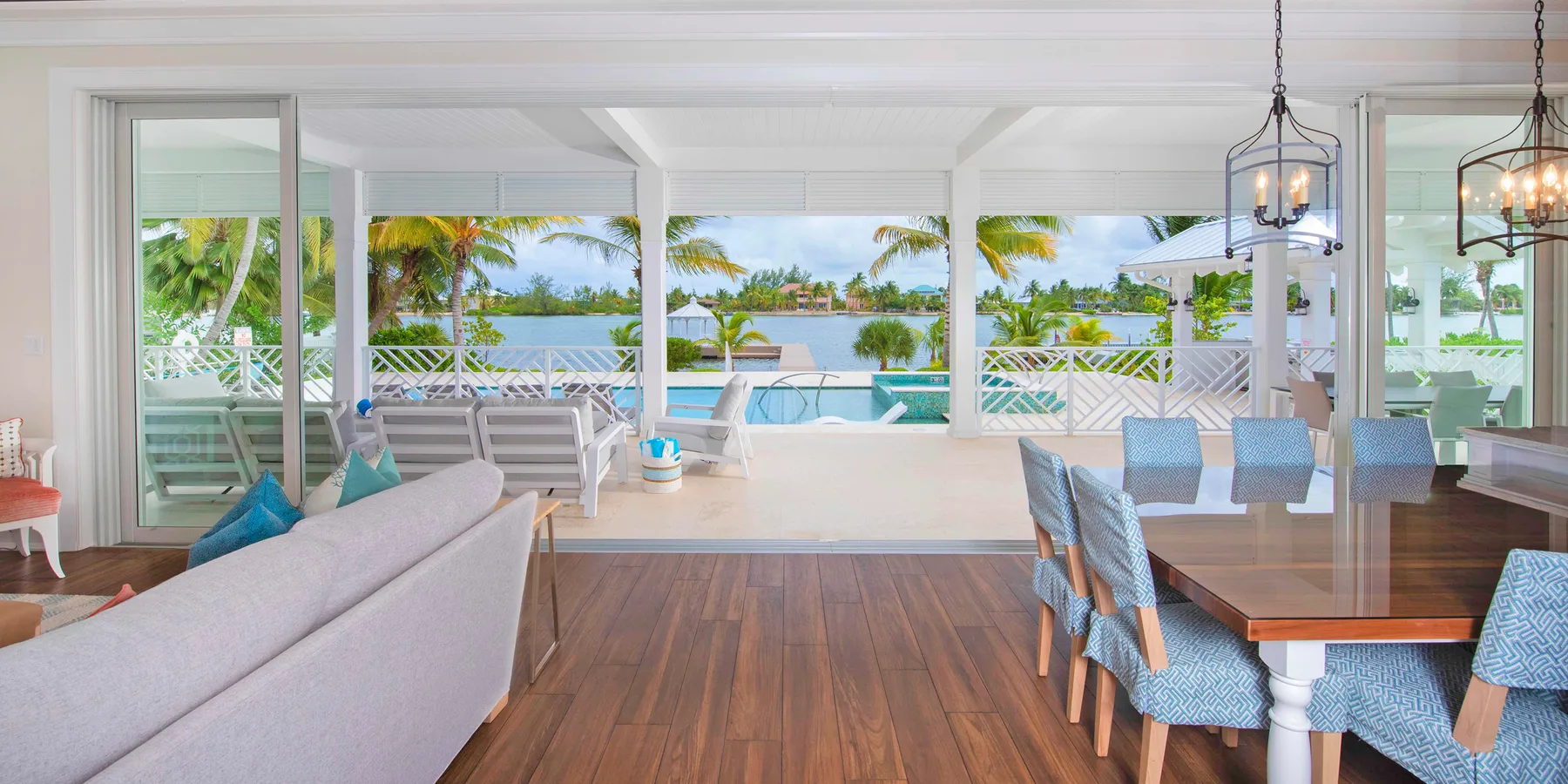 An open living and dining area faces a patio, pool, and tropical greenery.