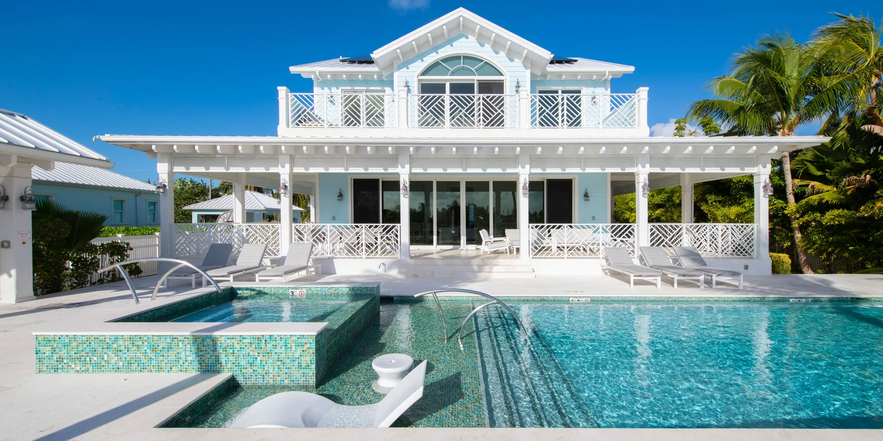 Una casa blanca da a una piscina con un spa elevado revestido de azulejos.