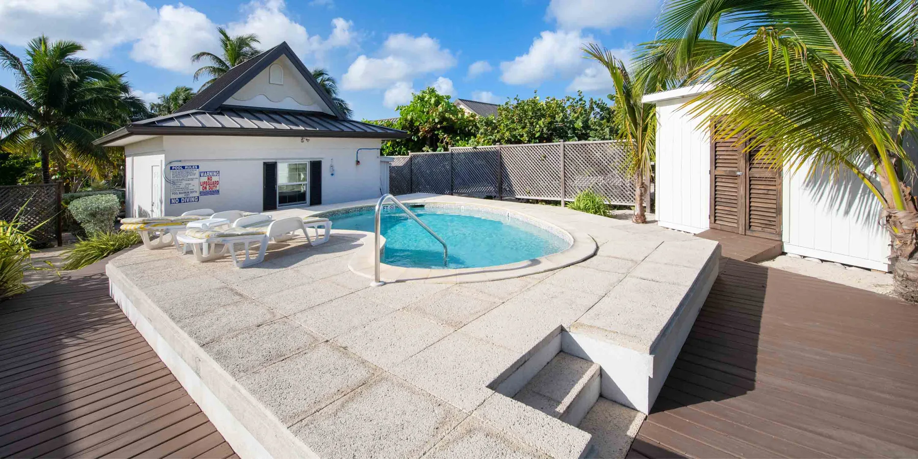 Una piscina al aire libre está en una terraza pavimentada elevada junto a un edificio pequeño.