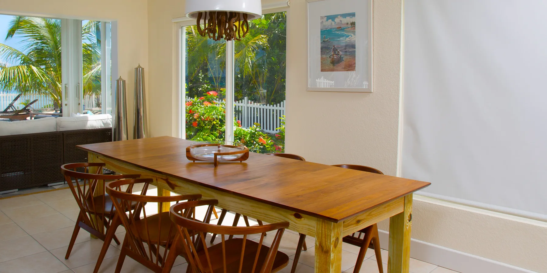 A bright dining area with a long wooden table and seating beside garden-facing windows.
