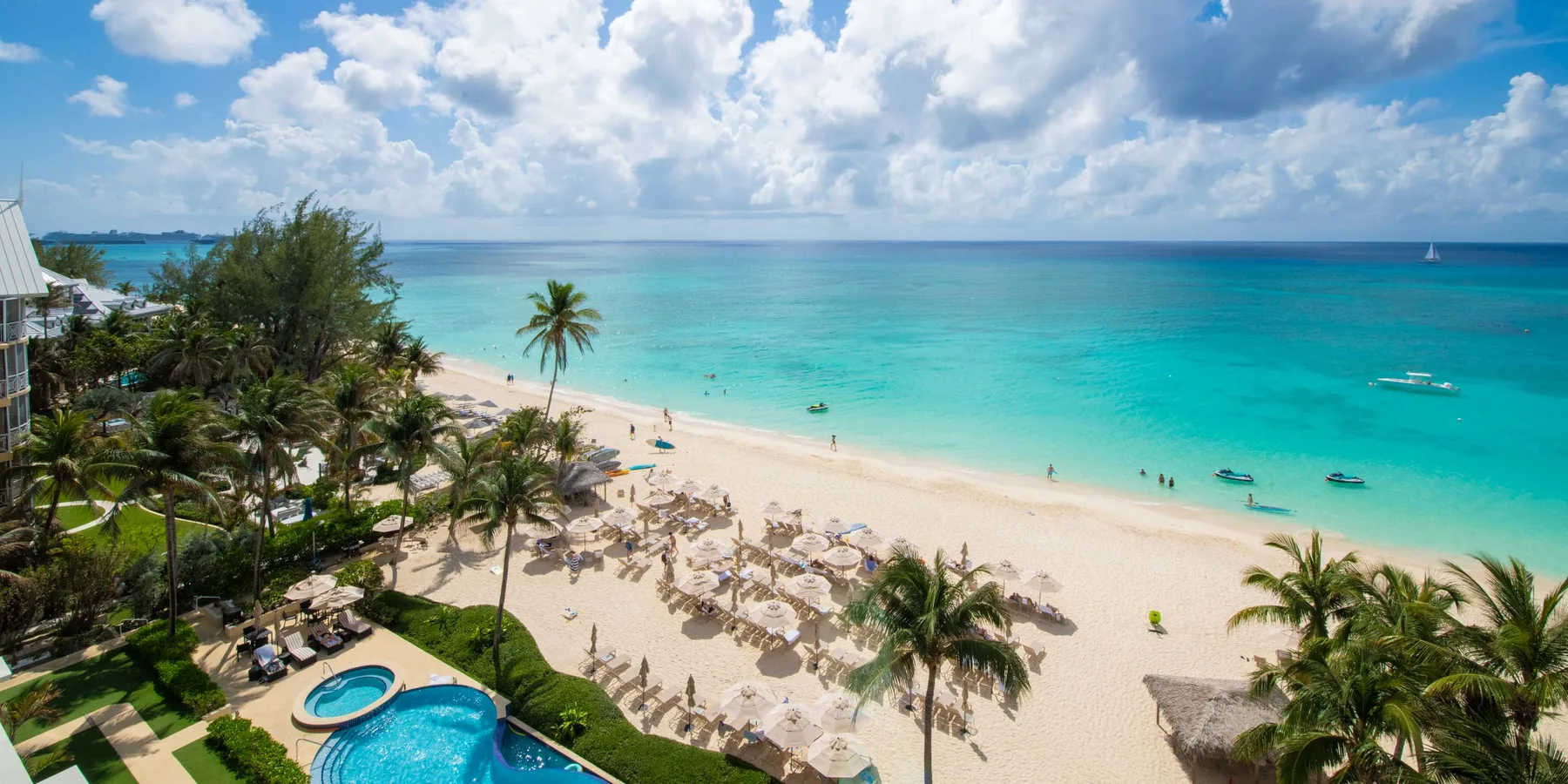 Una playa tropical y un océano turquesa se ven junto a un complejo bordeado de palmeras.