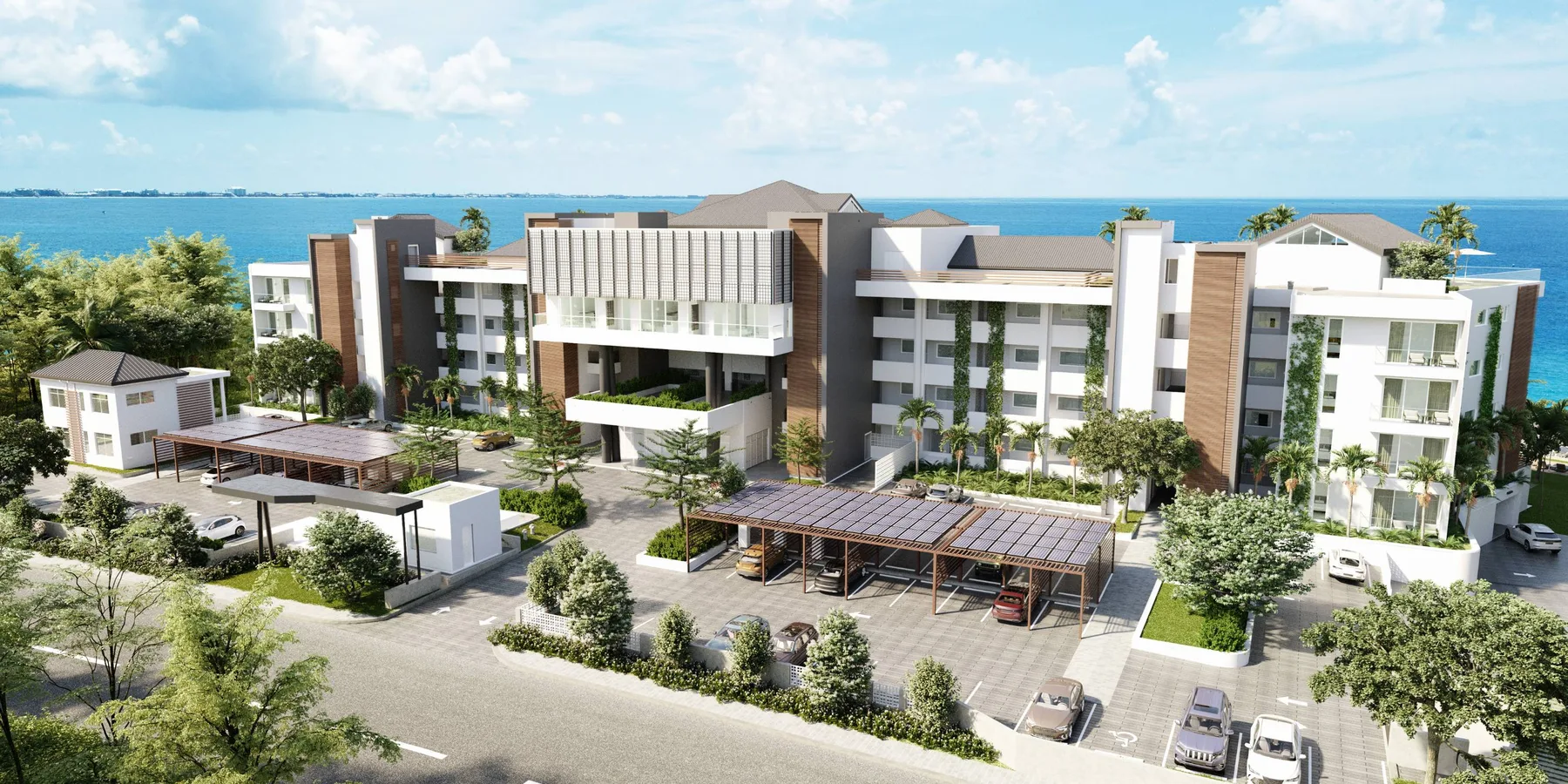 A modern multi-story building stands beside a landscaped parking area, with the sea visible behind it.
