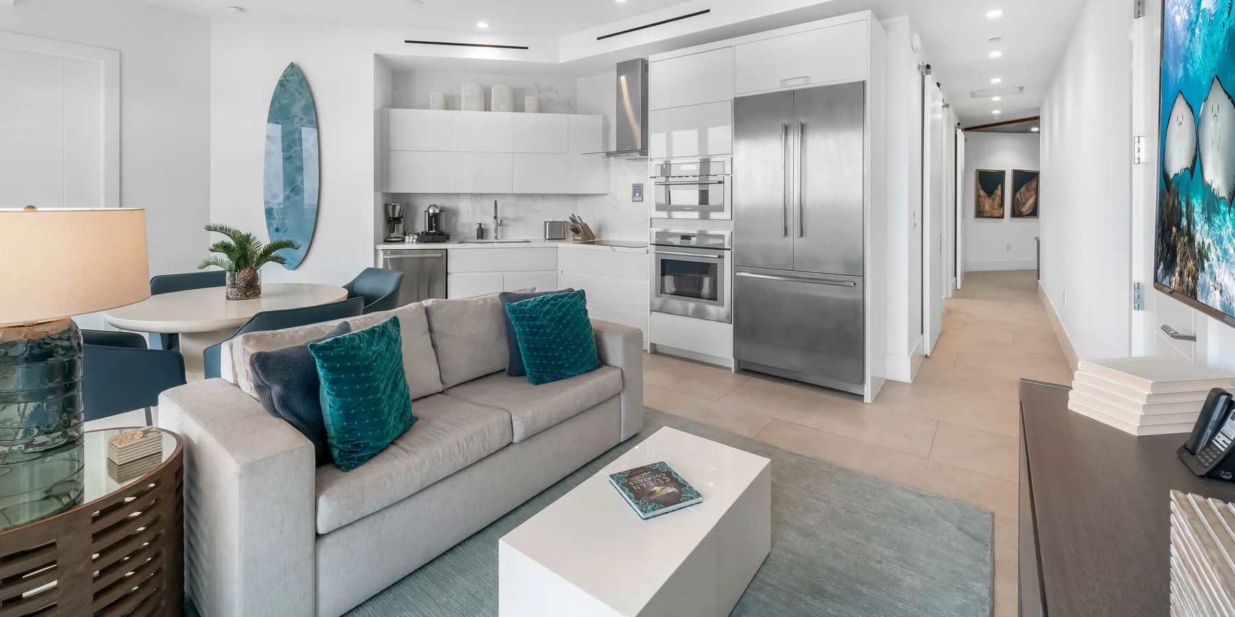 Una luminosa sala de estar de planta abierta con asientos, mesa de comedor y cocina blanca.