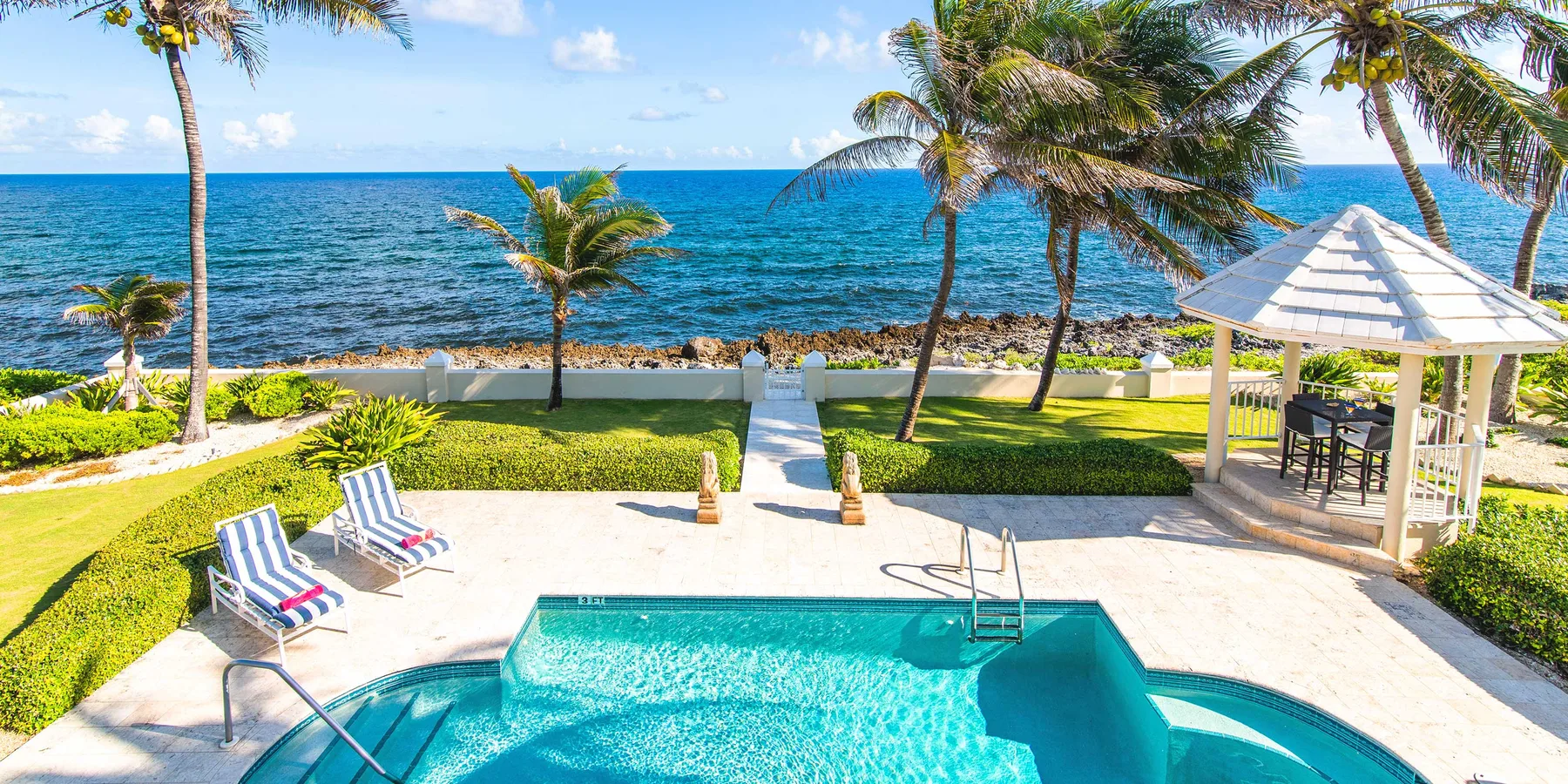 A swimming pool and lounge chairs overlook the ocean.
