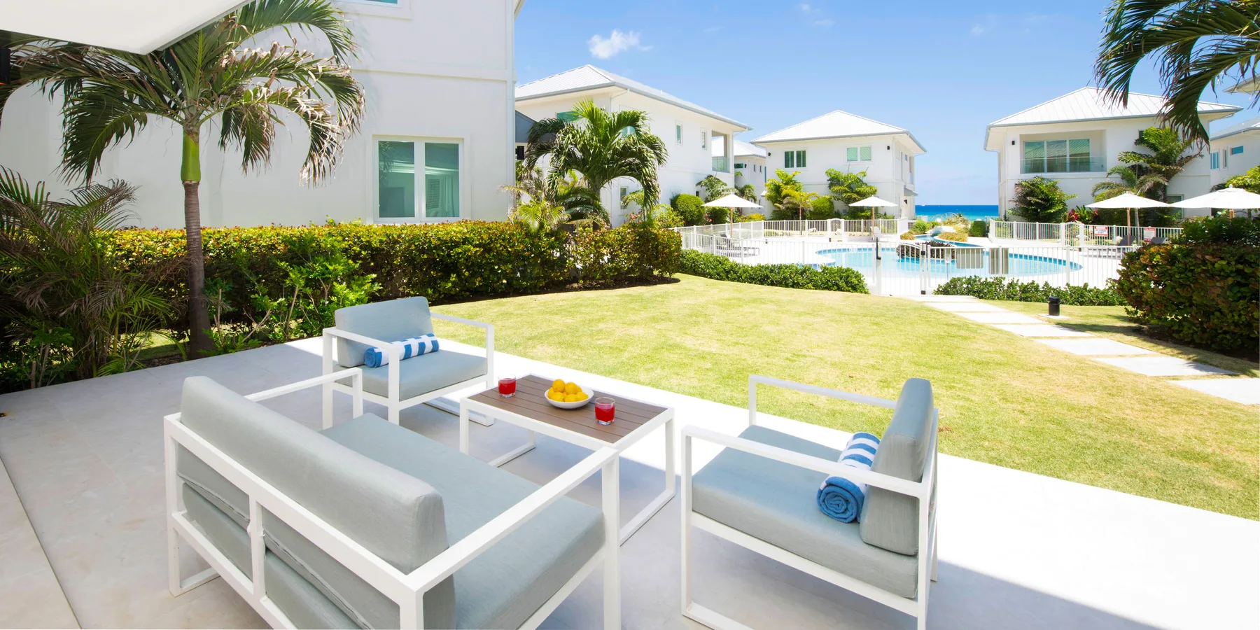 Outdoor patio seating overlooks a lawn, pool, and nearby buildings.
