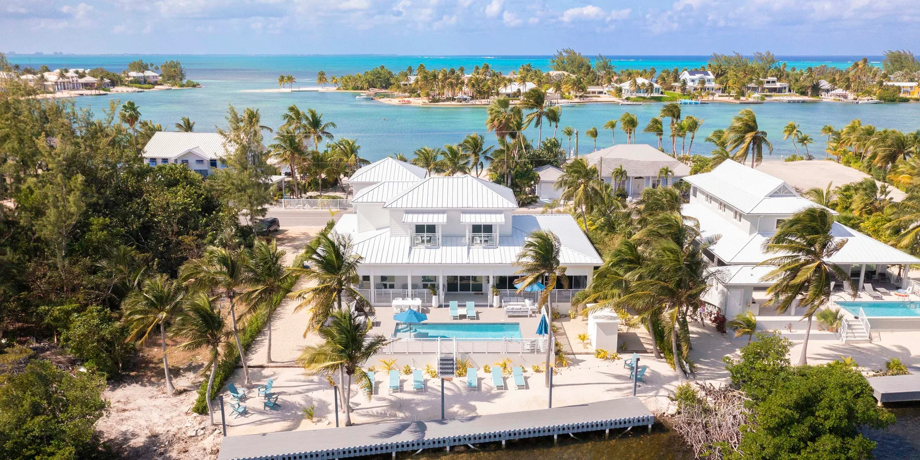Aerial view of waterfront homes and pools beside a turquoise bay.