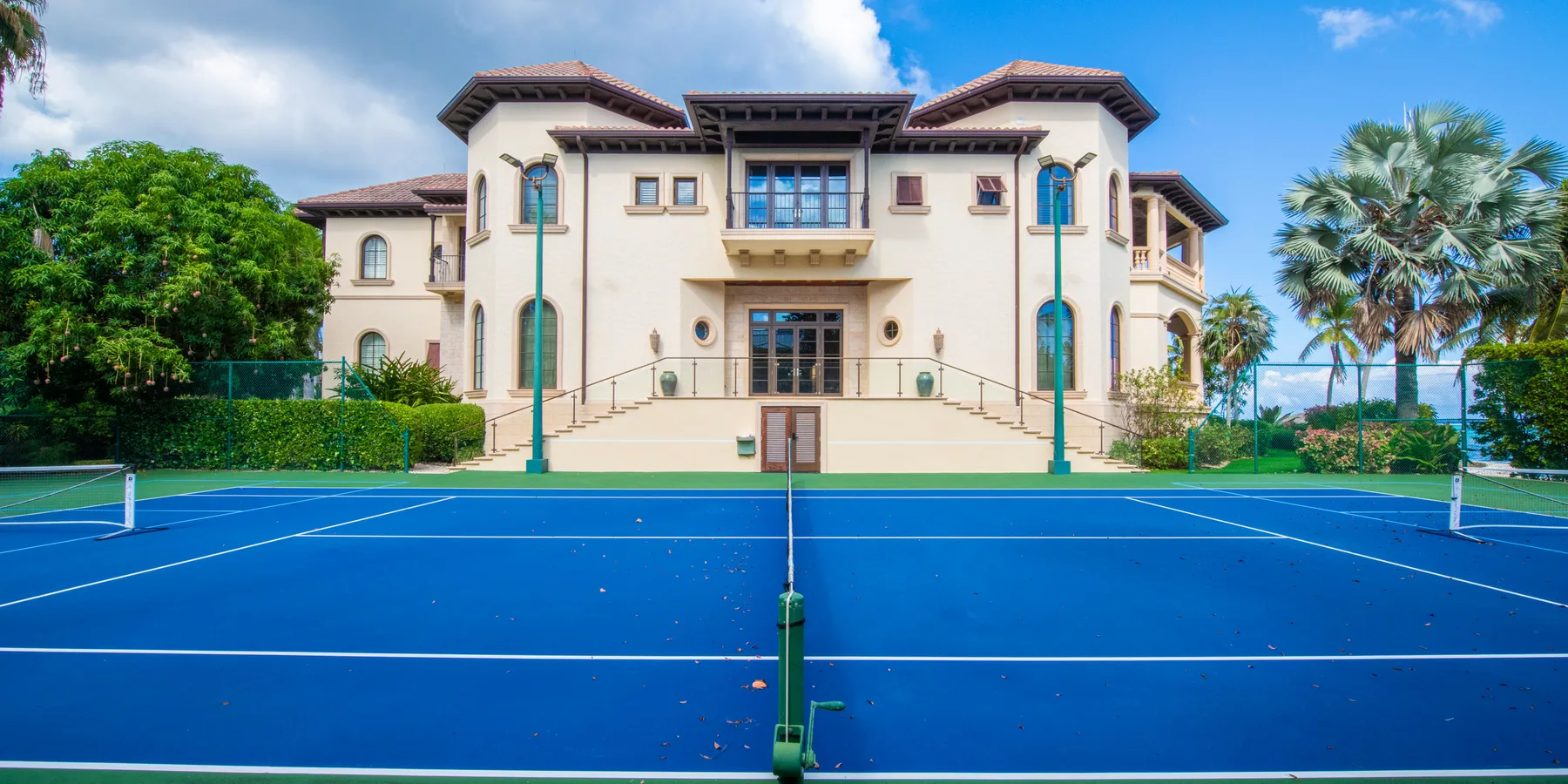 Una cancha de tenis azul está frente a un edificio grande, con palmeras cerca.