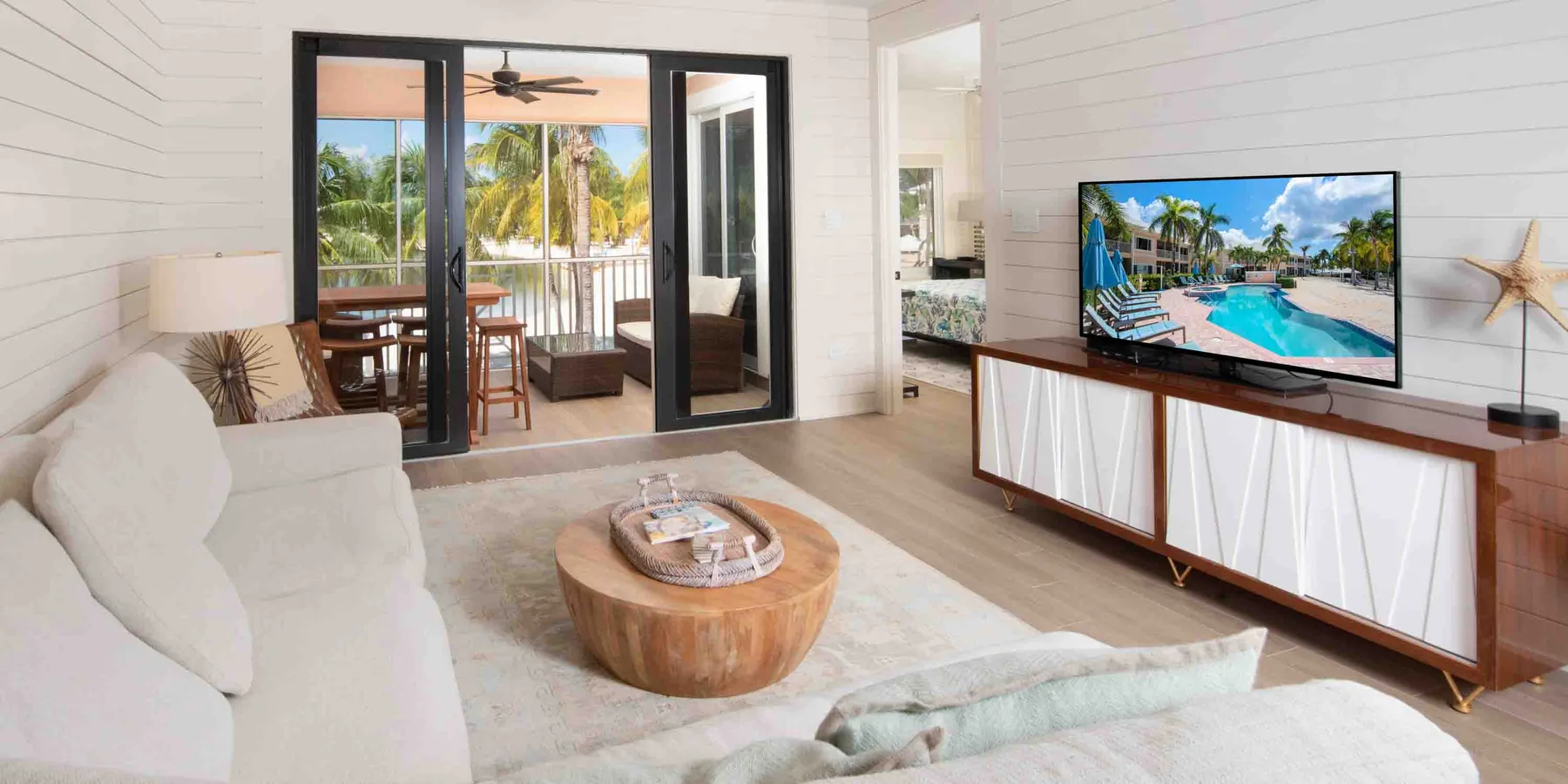 A bright living room with seating, a round wooden coffee table, and a television.