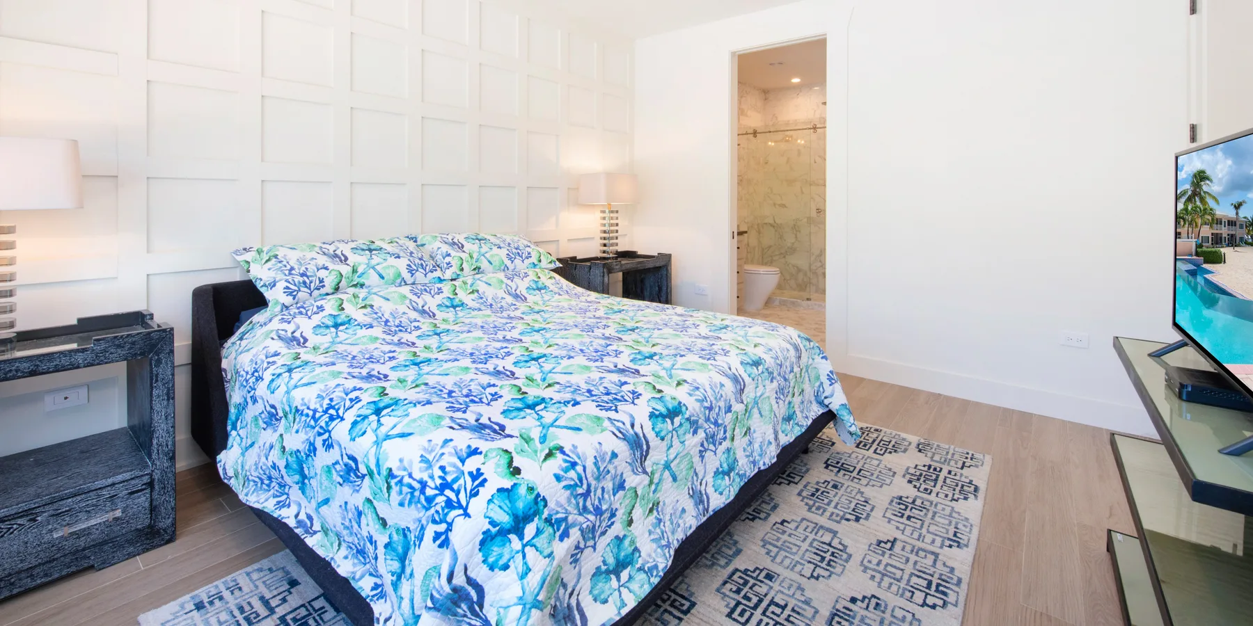 A bedroom with a bed covered in blue and green floral bedding.