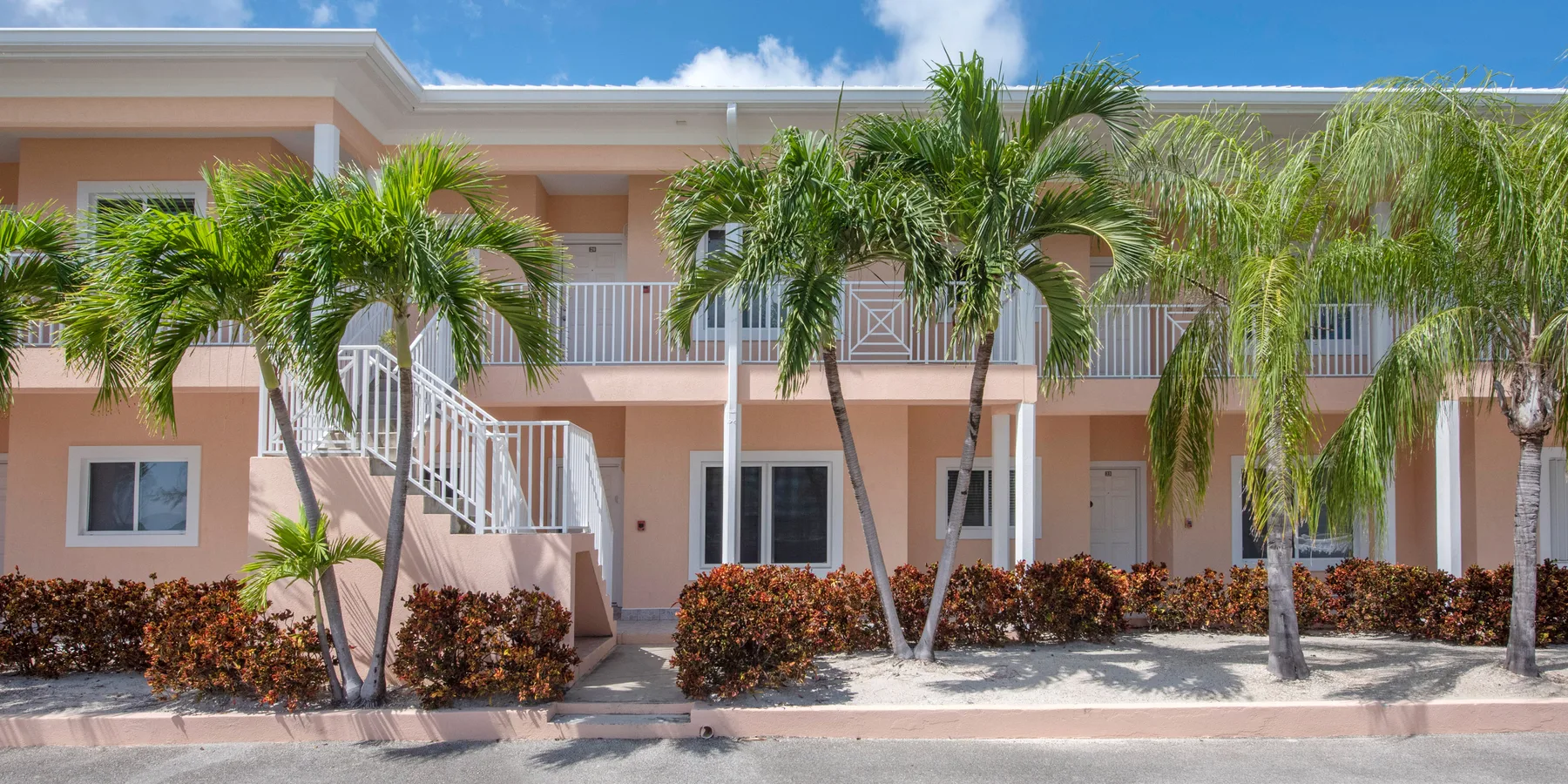 A two-story apartment building with balconies and palm trees in front.