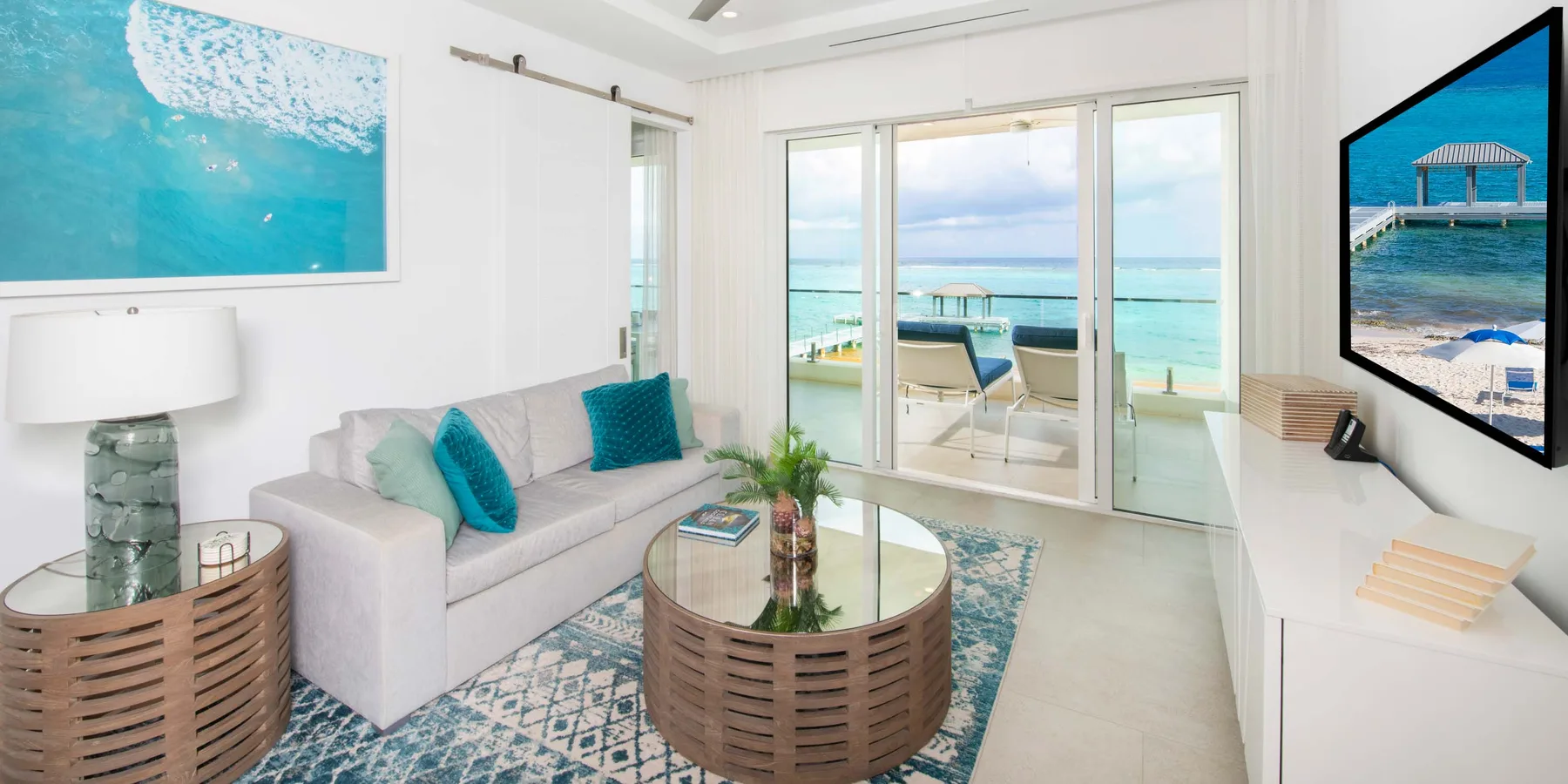Una sala luminosa con asientos y una mesa de centro de vidrio junto a ventanas con vista al mar.