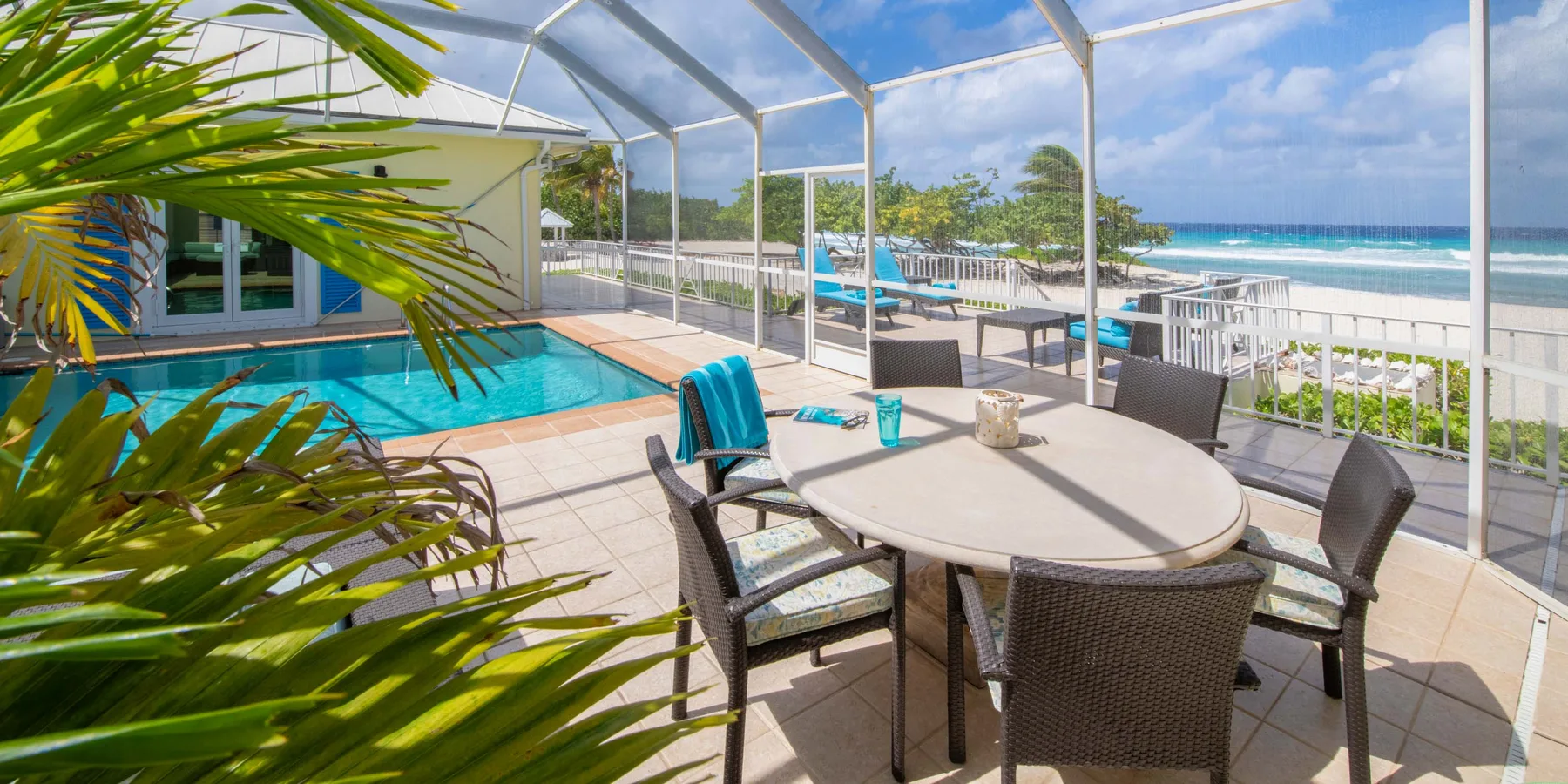 Un patio cubierto con mesa de comedor da a una piscina y a la playa.