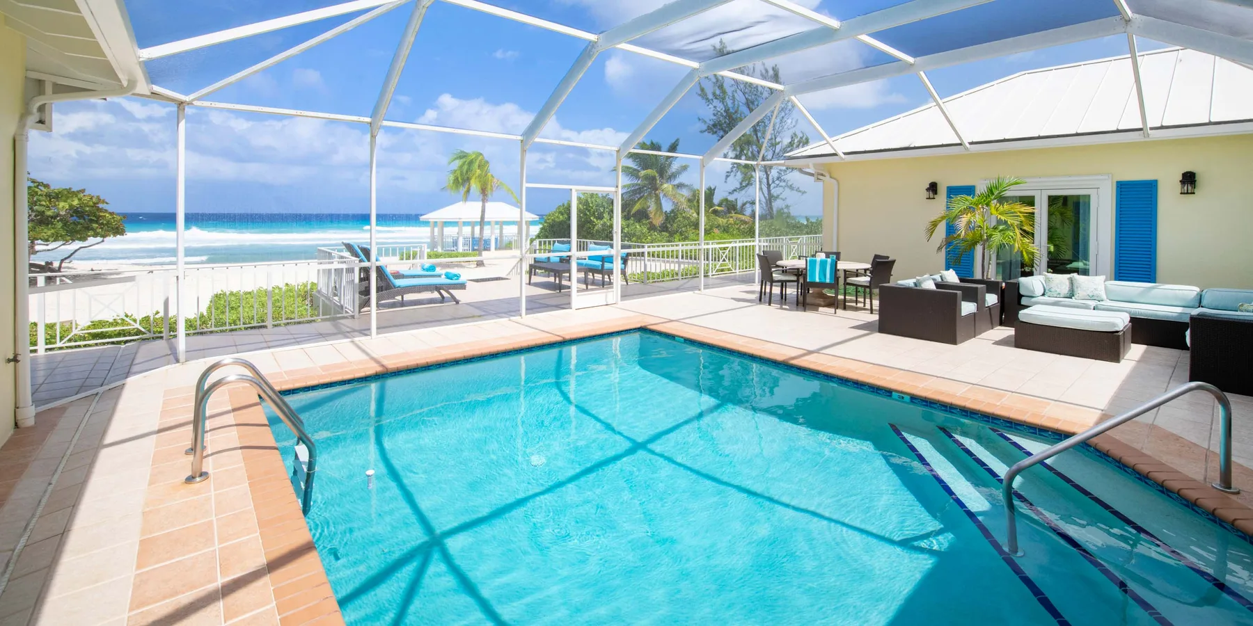 Una zona de piscina con malla, asientos en el patio y vista al mar.