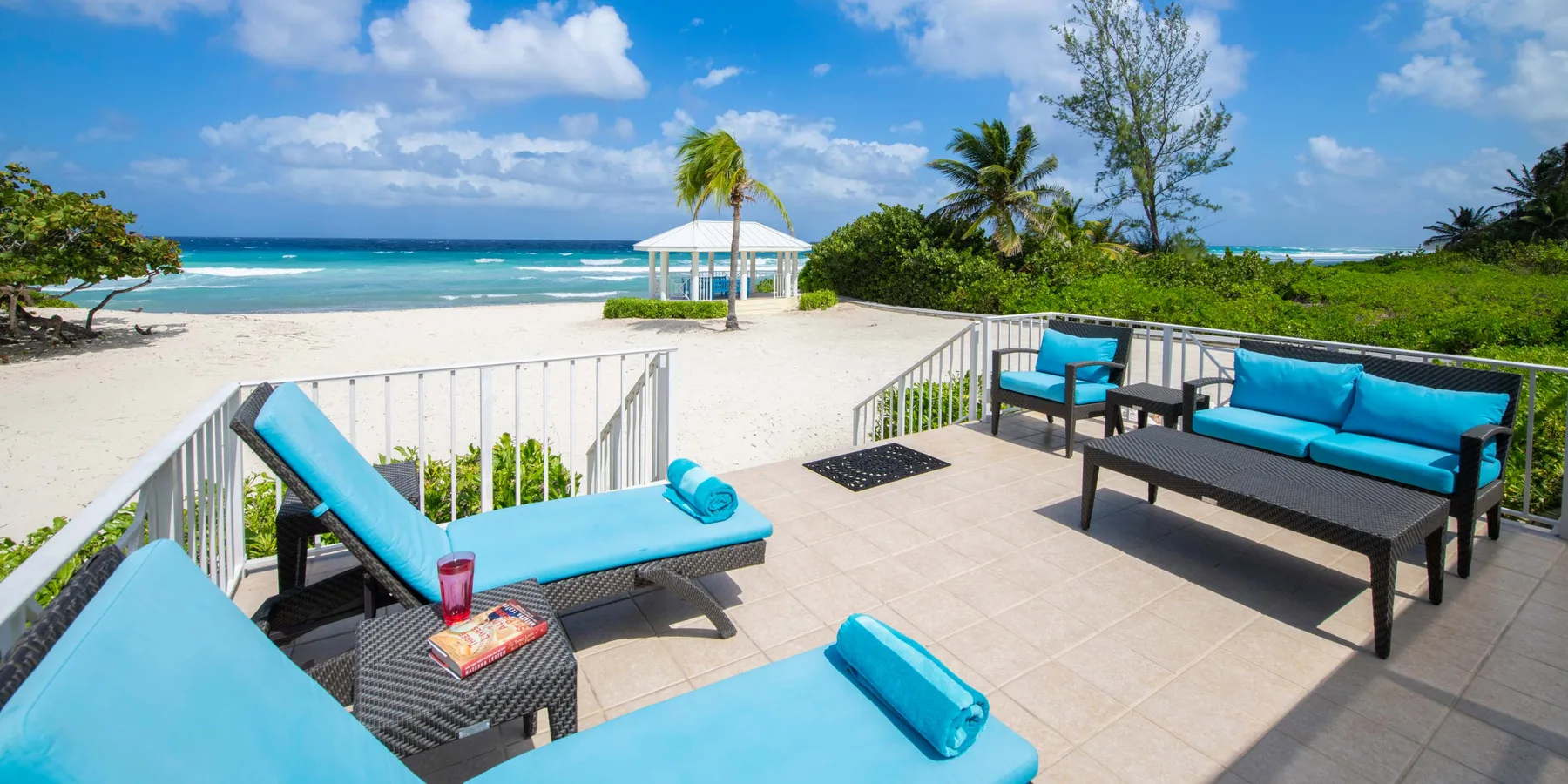 Un patio con asientos azules da a una playa de arena y al océano.
