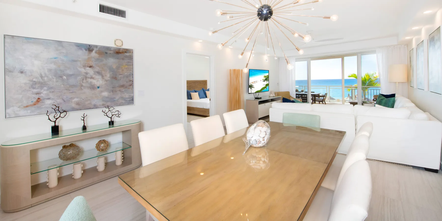 Una luminosa sala de estar y comedor diáfanos, con una mesa grande de madera y vistas al mar.