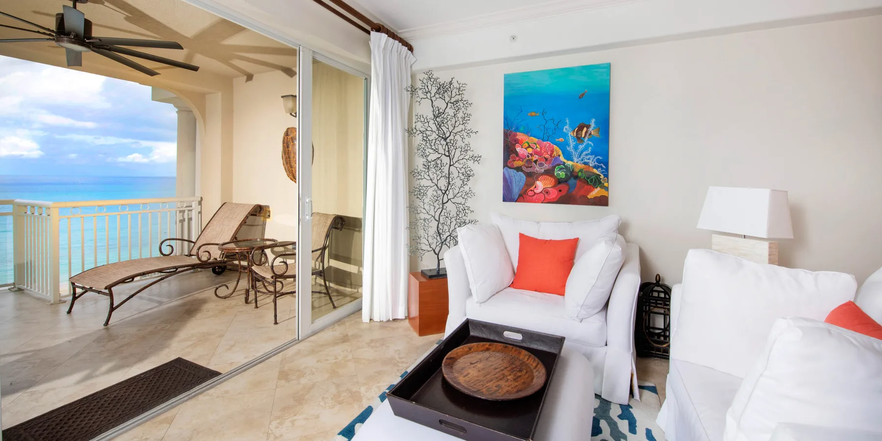 Una sala luminosa da a un balcón con vistas al mar y arte colorido en la pared.