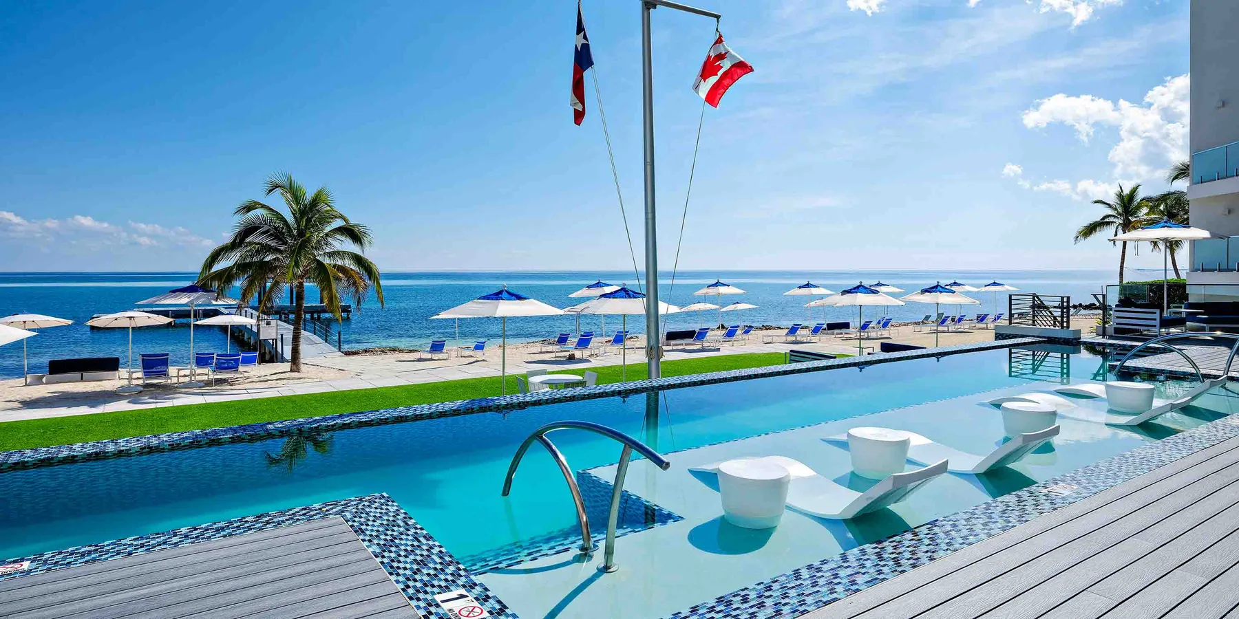 Una piscina junto al mar da al océano, con asientos bajo sombrillas a la orilla.