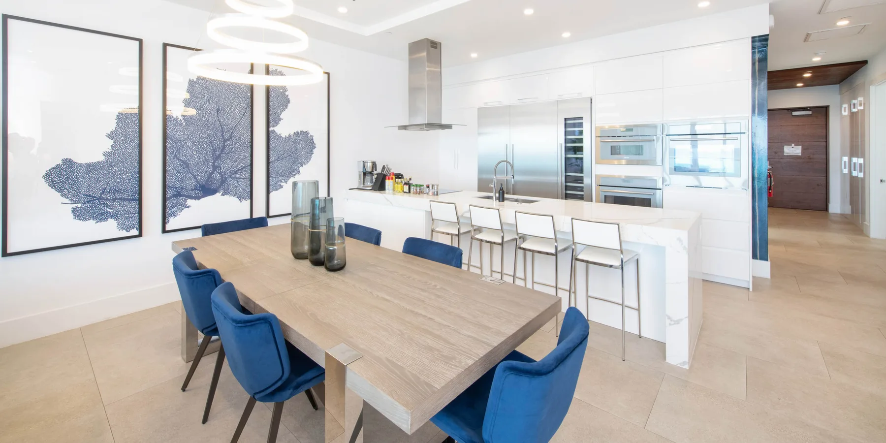 Un comedor luminoso con una mesa de madera y asientos azules junto a una cocina moderna.