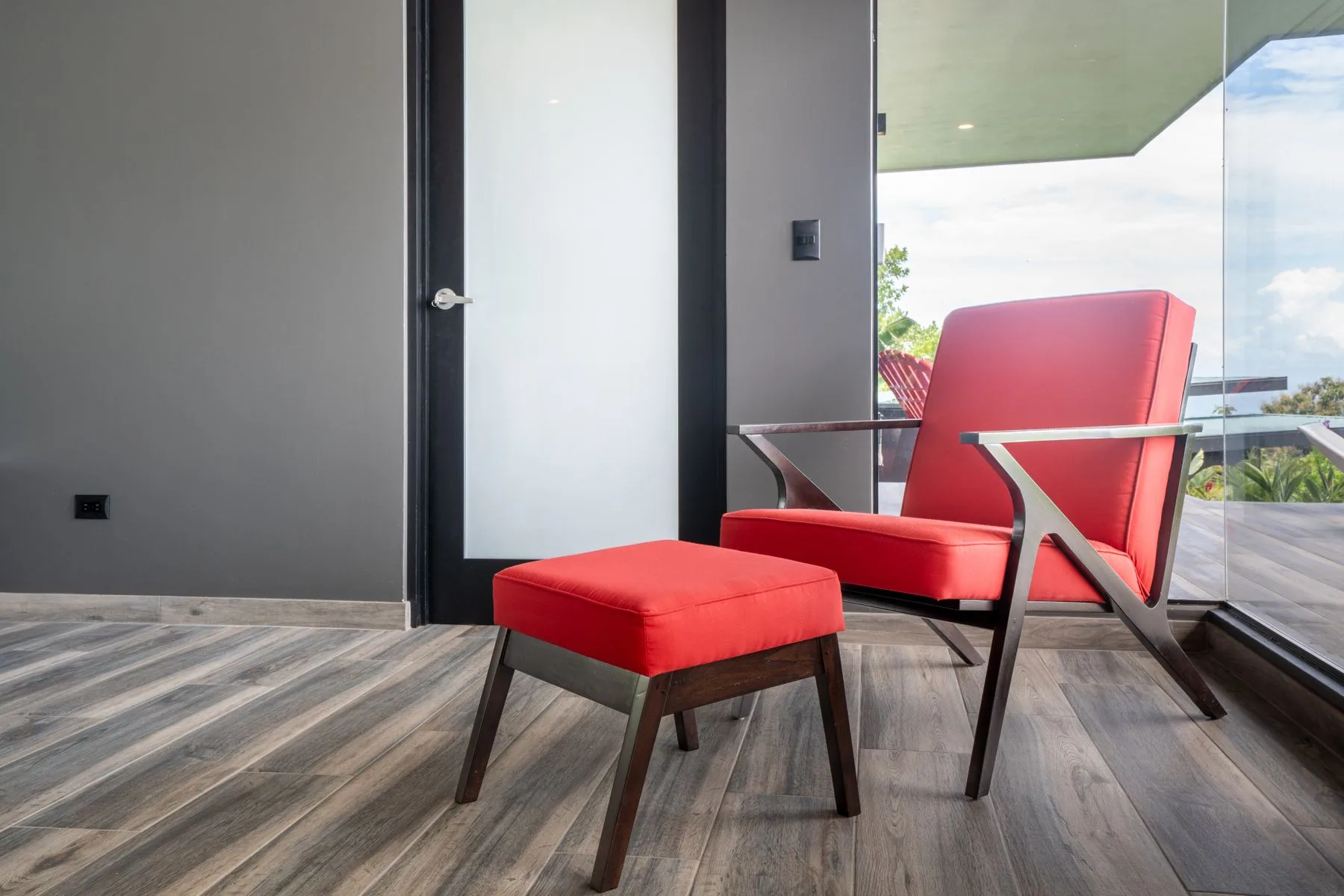 A red lounge chair and matching ottoman sit beside a glass balcony door.