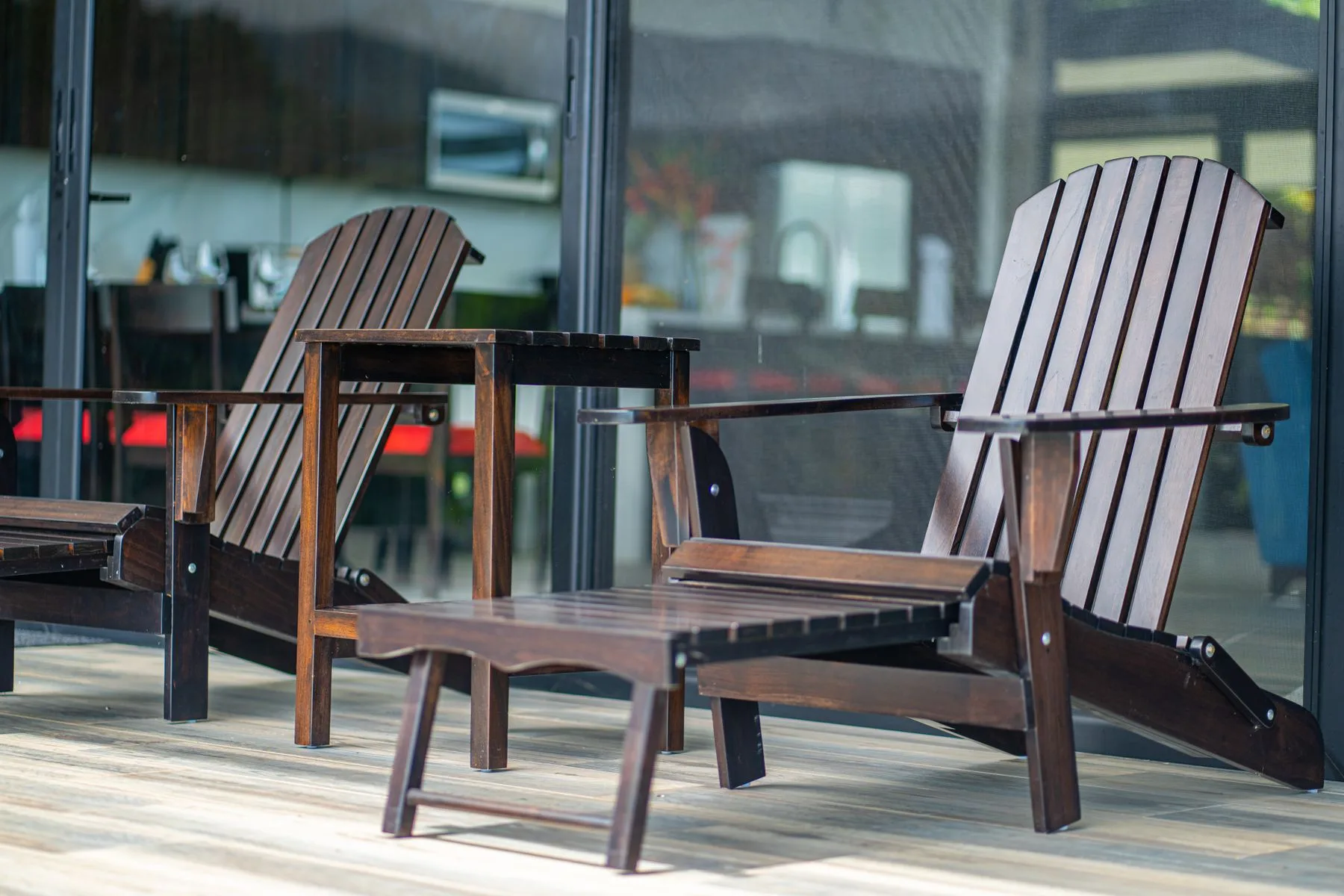 Outdoor seating sits on a wooden deck beside large glass windows.