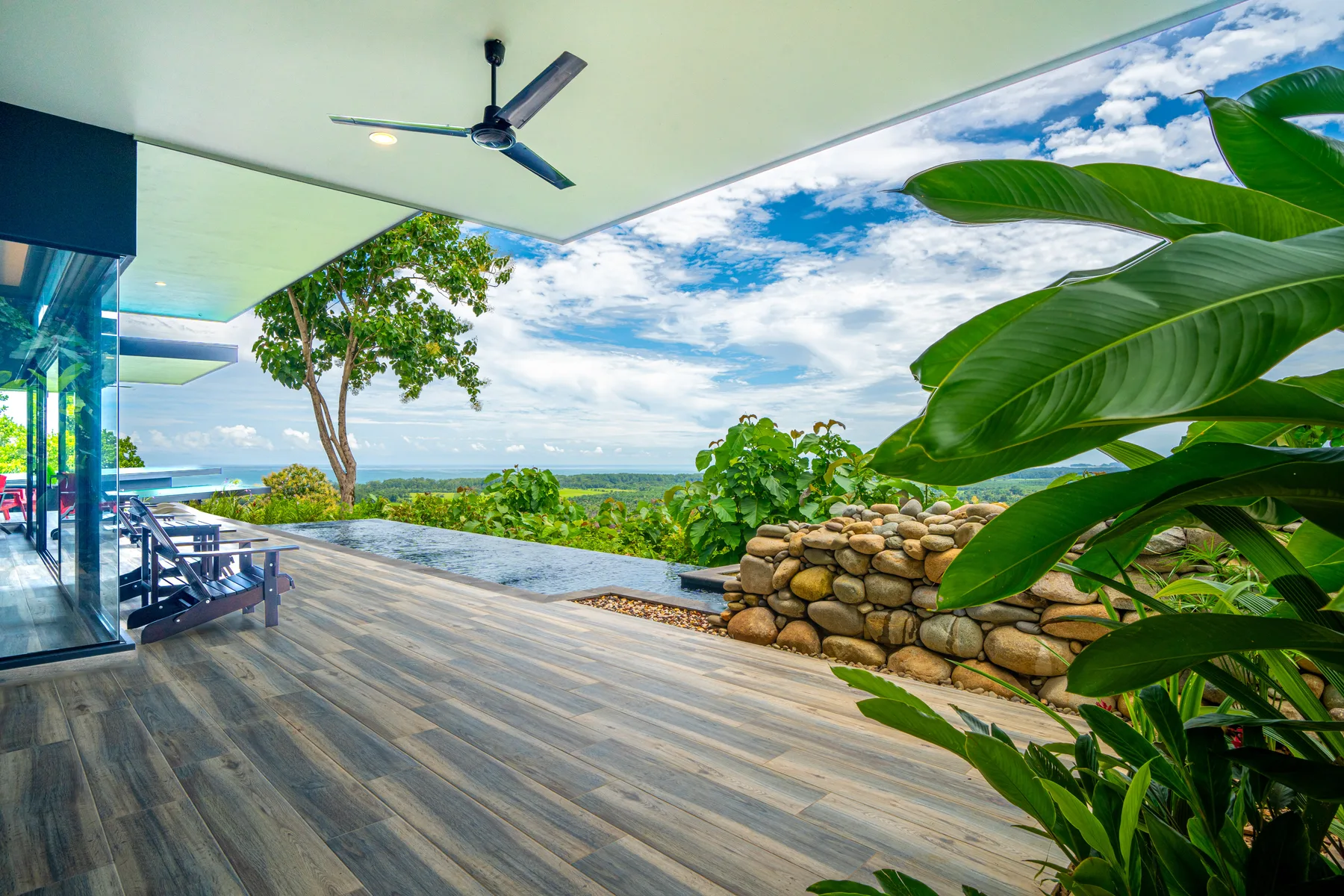 A covered outdoor terrace overlooks a green landscape, with leafy plants along the edge.