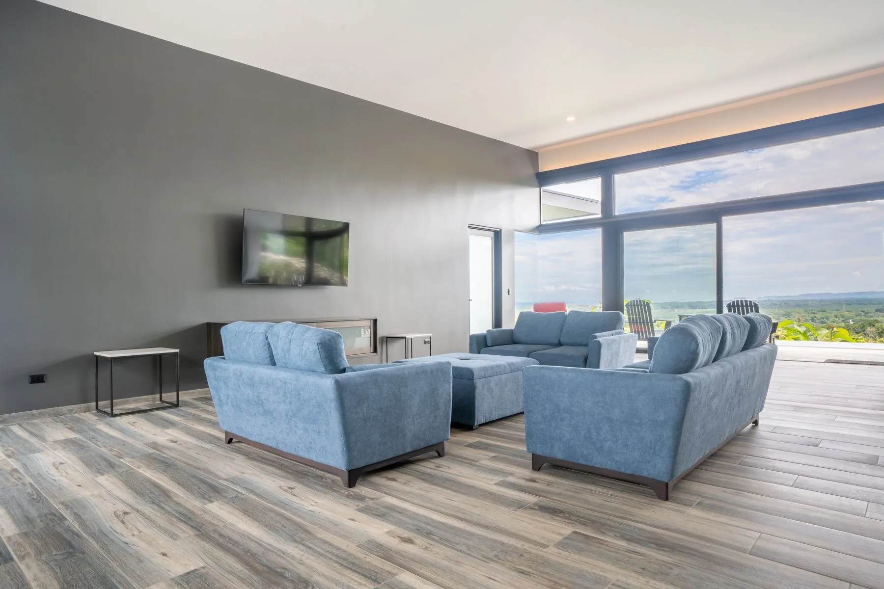 A living room with blue seating and large windows overlooking the landscape.