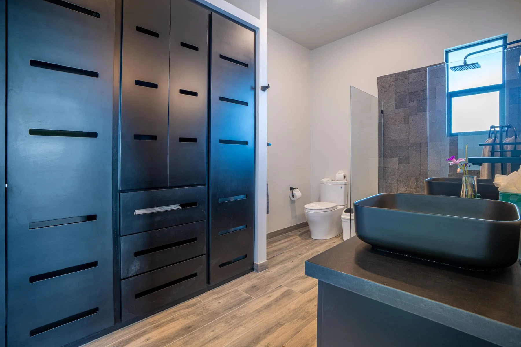 A modern bathroom with a dark bathtub, toilet, and built-in cabinetry.