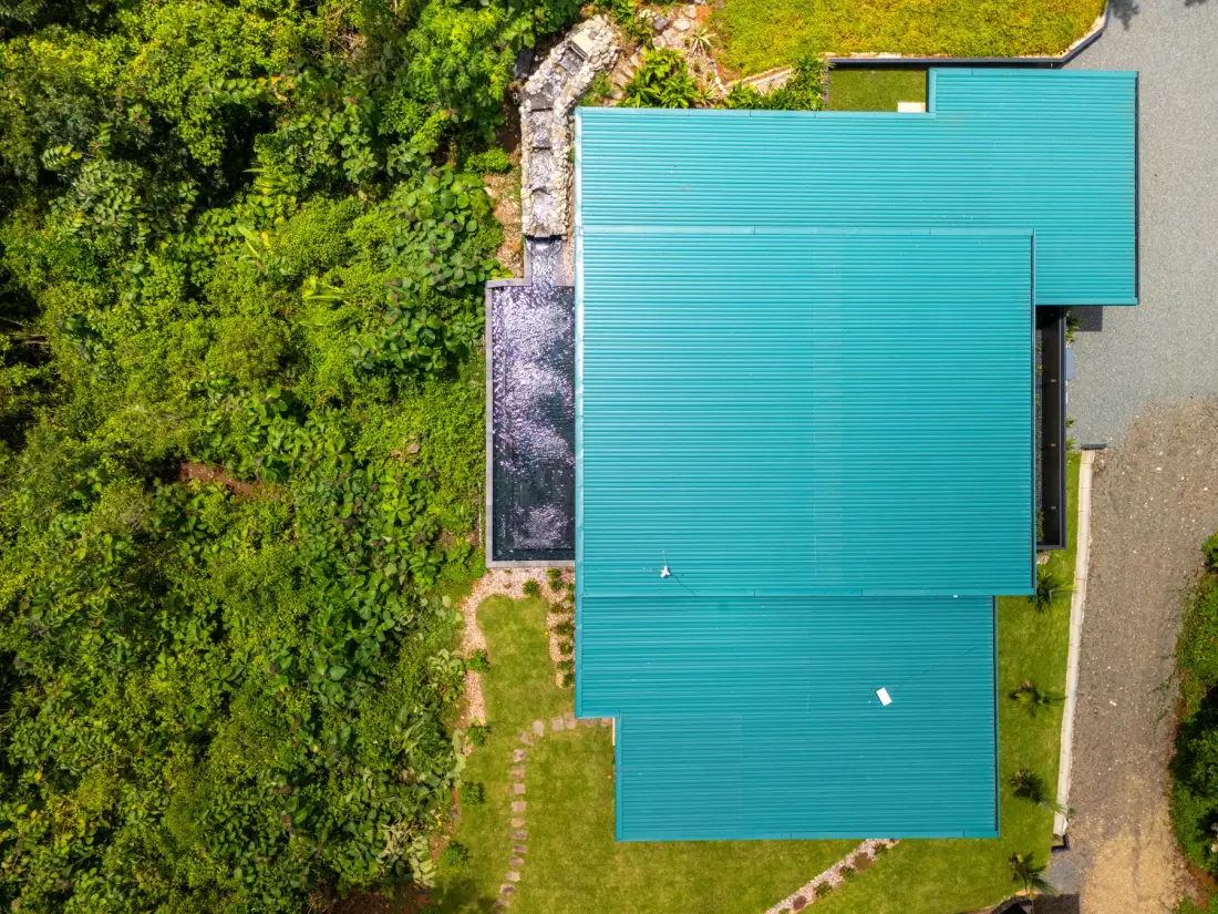 An aerial view of a turquoise-roofed building beside dense greenery.