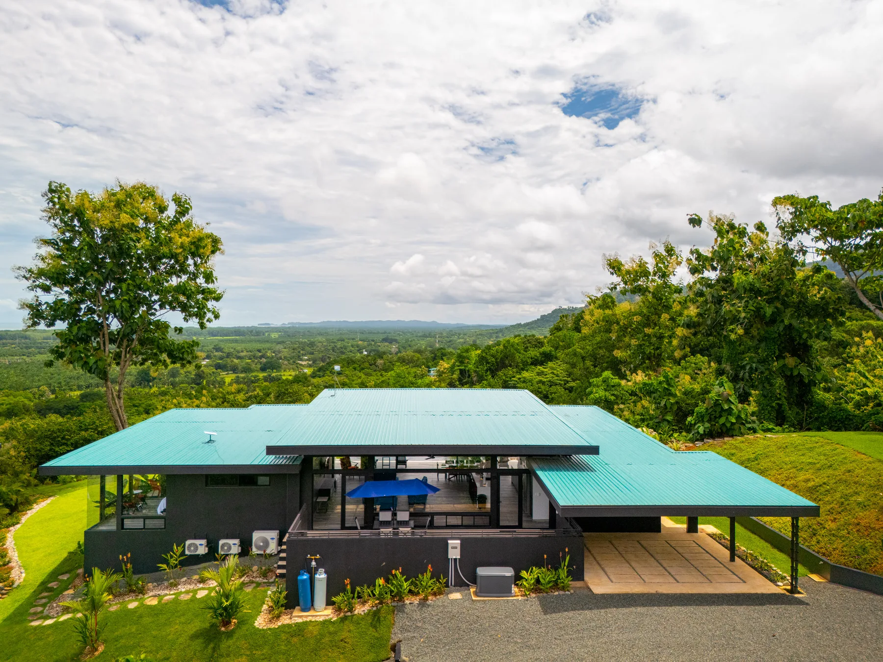 A modern building with a turquoise roof overlooks a green, wooded landscape.