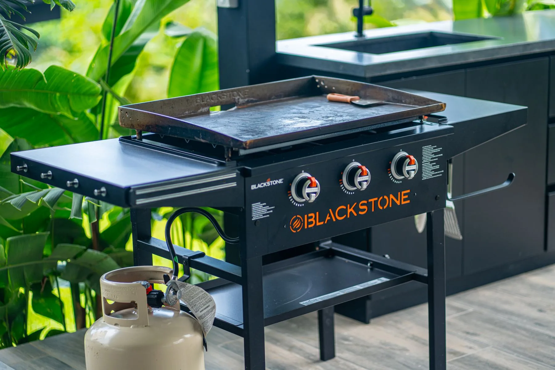 An outdoor cooking station with a flat-top griddle and propane tank.